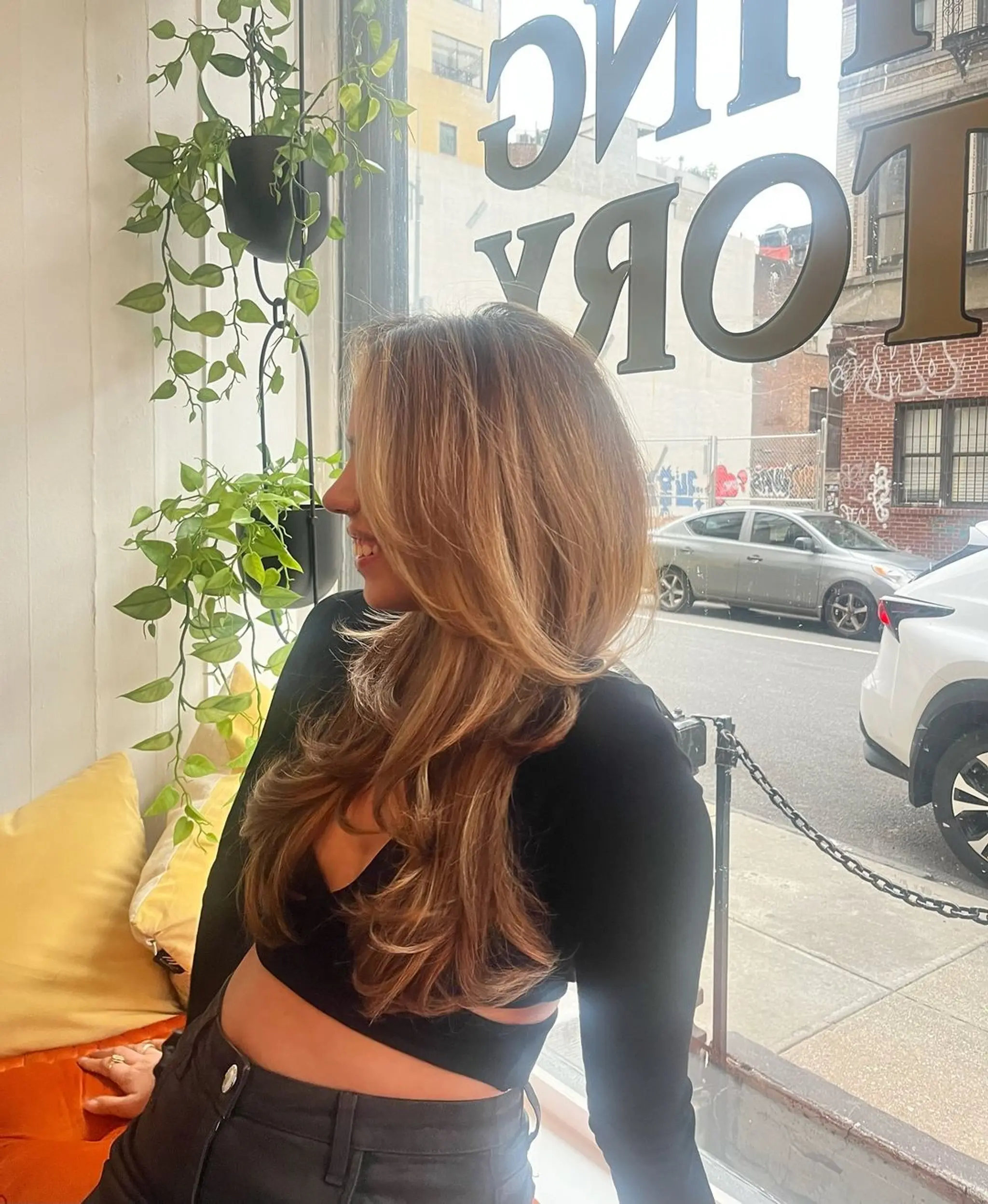 Long, wavy hair with layered cuts that add volume and face-framing dimensions. The color is a mix of blonde and light brown, giving a natural, sun-kissed appearance.