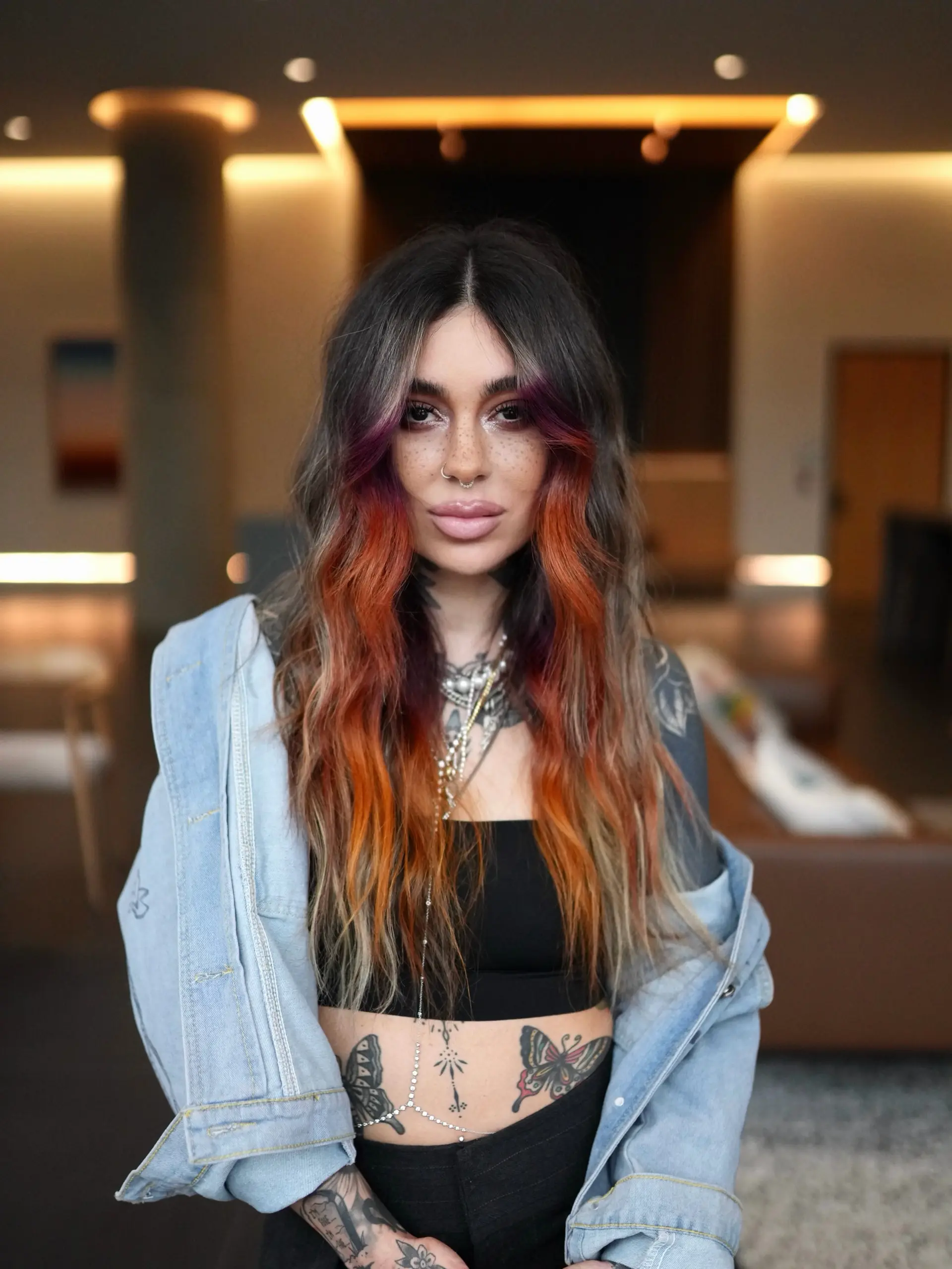 Long wavy brunette hair featuring a vibrant sunset-inspired money piece blending purple, coral, and bright orange tones. 1