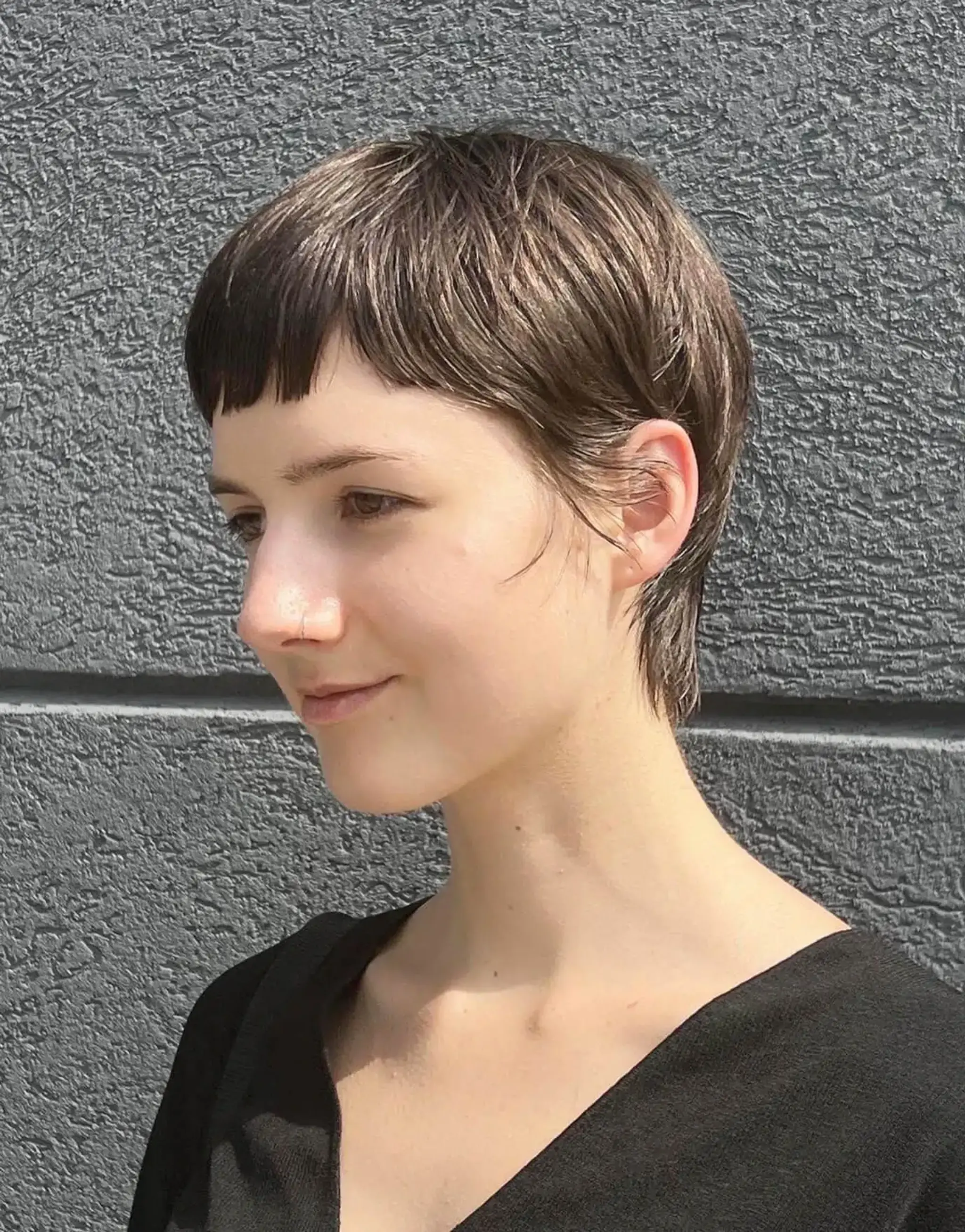 A chic crop cut with dark brown straight hair, styled into a short pixie with short layered lengths and a subtle fringe.
