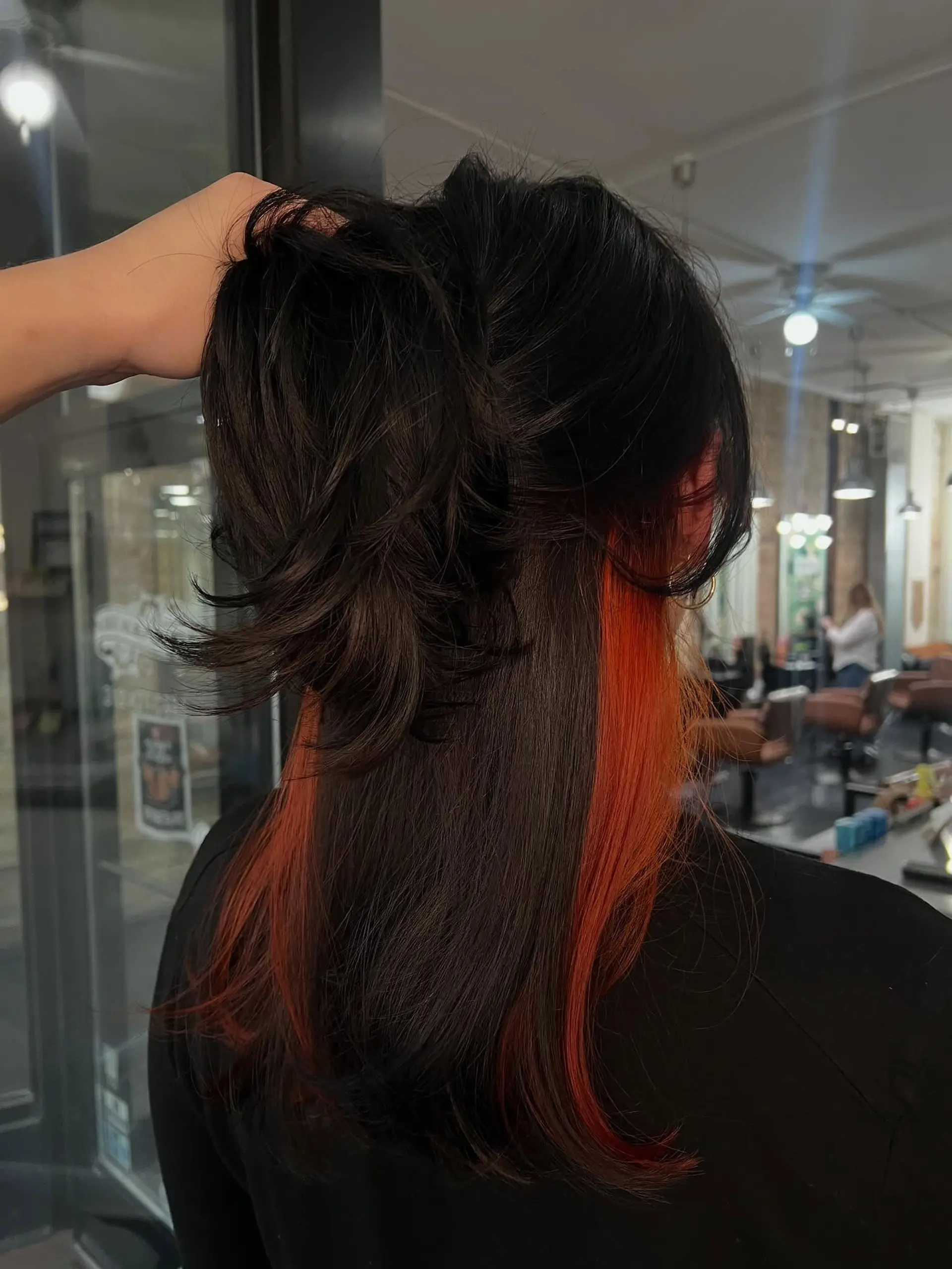 Straight dark hair styled to reveal vibrant pumpkin orange peekaboo underlights beneath the surface layer. 1