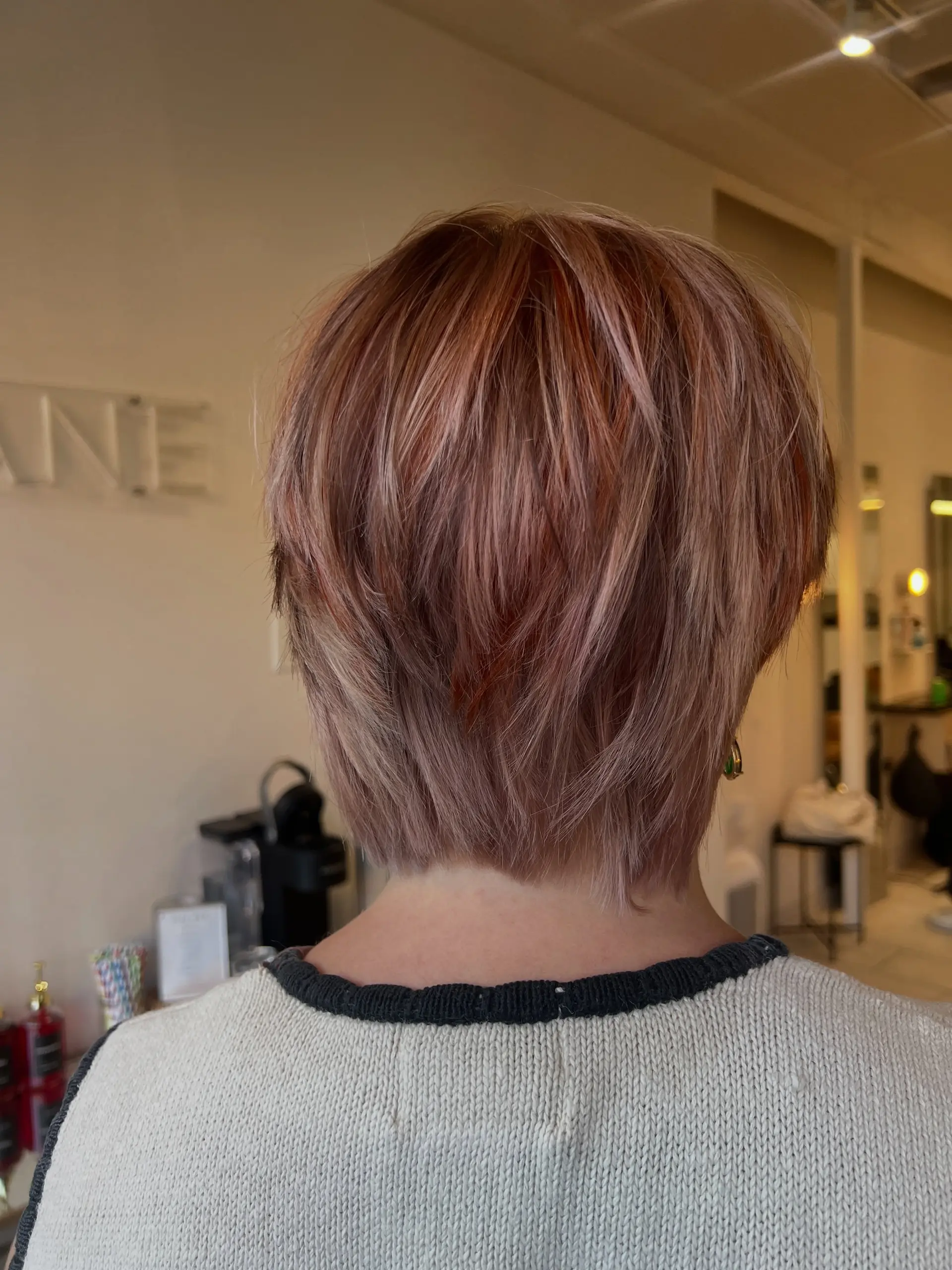 A textured short bixie haircut styled with dimensional calico tones blending soft dusty rose, copper, and blonde highlights. 1