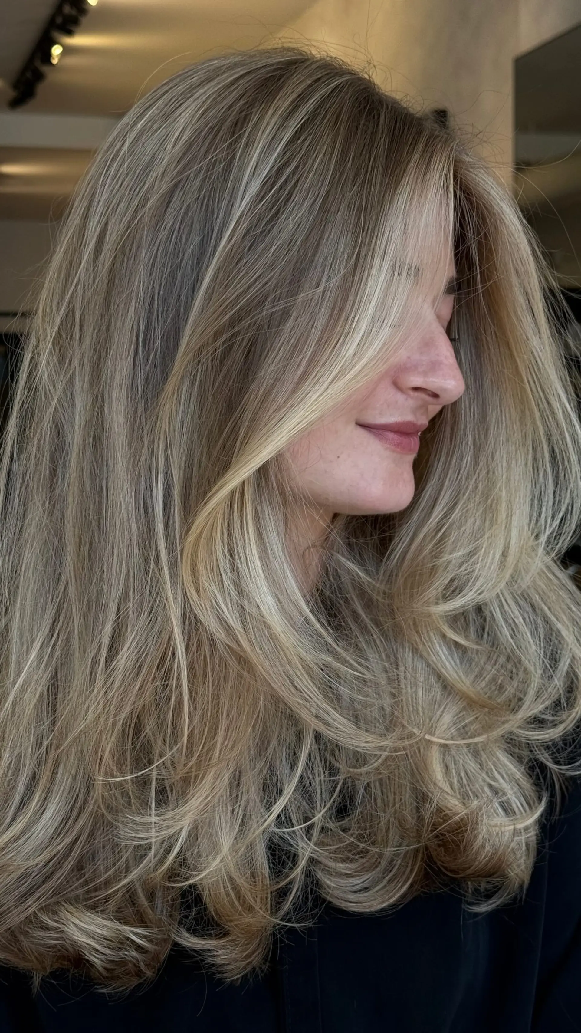 Long dimensional blonde hair styled with tiered face-framing layers and a soft, bouncy blowout. 1