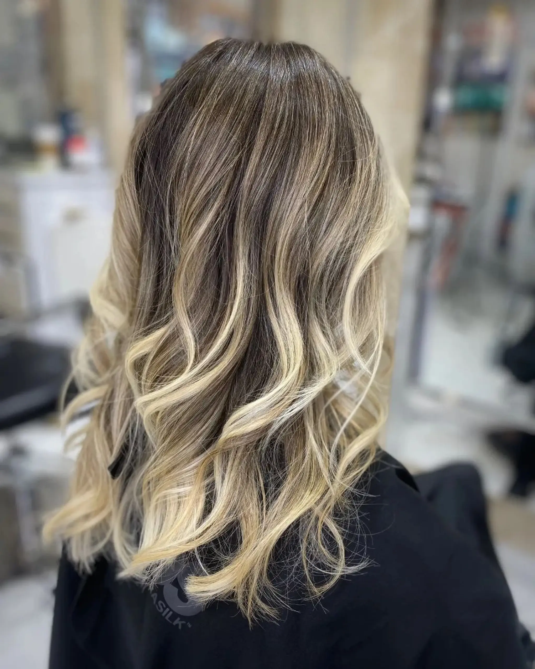 Medium-length, wavy ombre hair with dark blonde roots transitioning to light and golden blonde, styled in beach waves and soft curls with layered cuts.