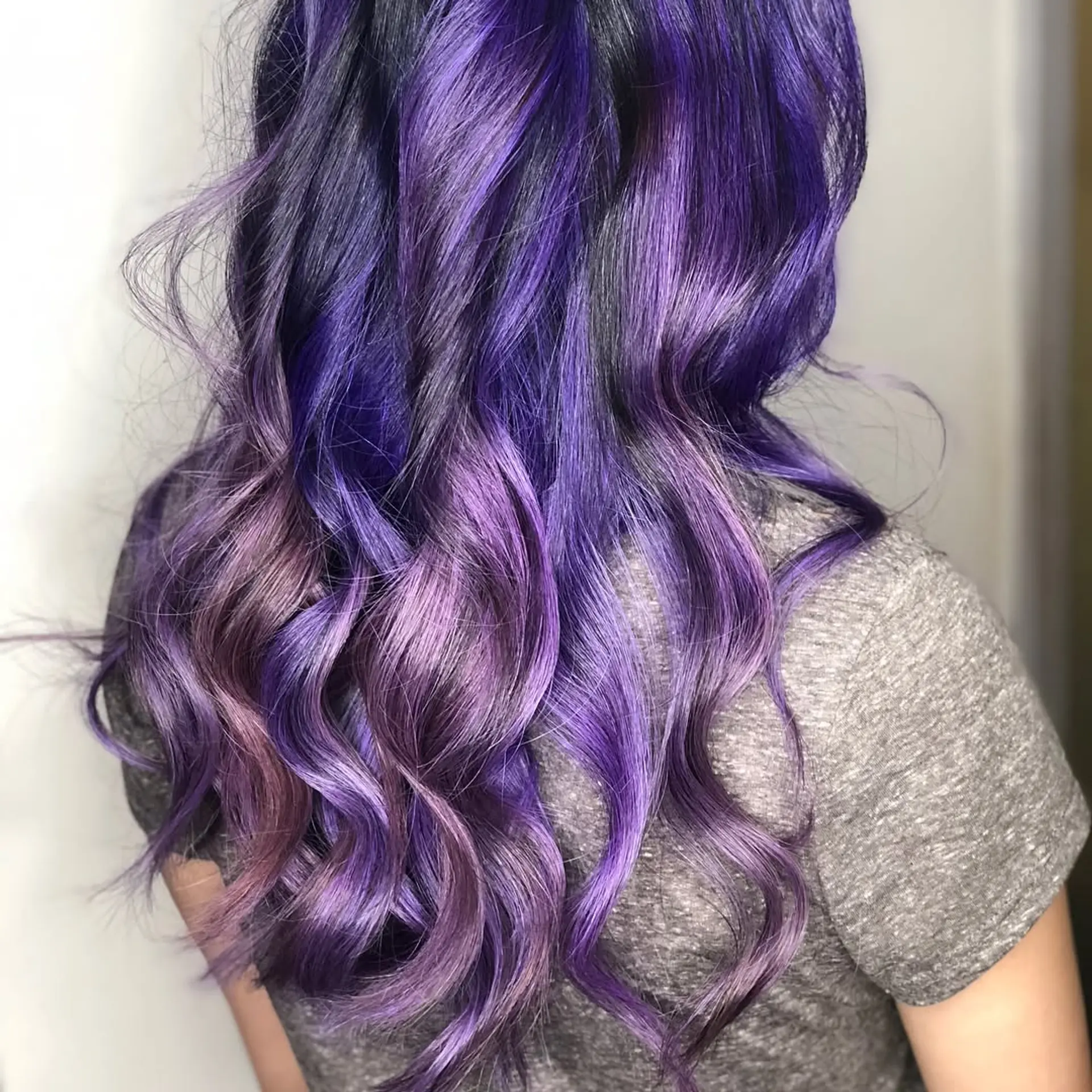 Long wavy hairstyle dyed in multi-dimensional shades of vivid violet and rich purple over dark roots. 1