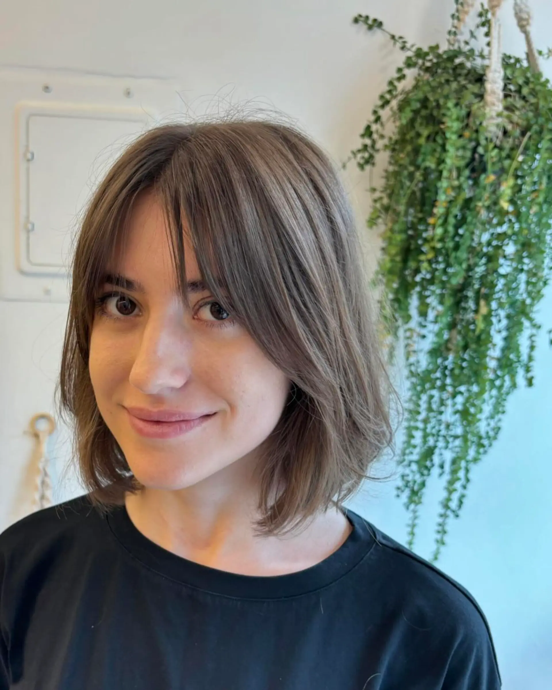 A medium-length, wavy cut in a soft brown color, featuring feathered bangs and lightly layered ends for a natural, casual look. 1