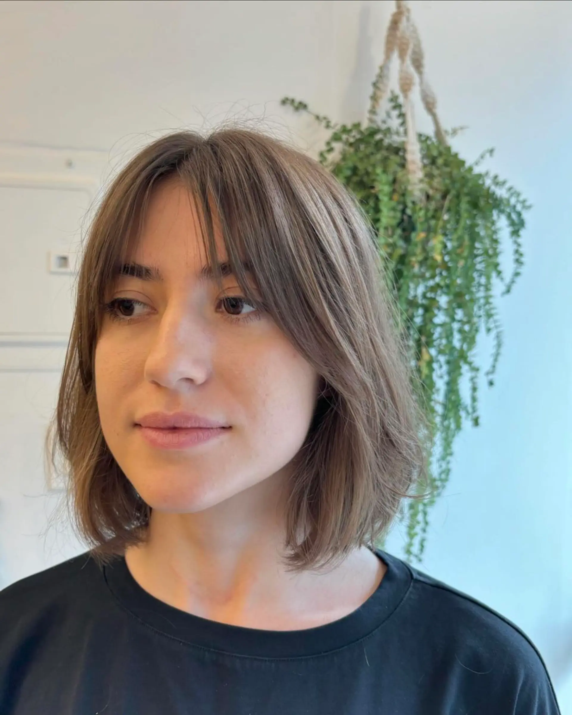 A medium-length, wavy cut in a soft brown color, featuring feathered bangs and lightly layered ends for a natural, casual look. 2