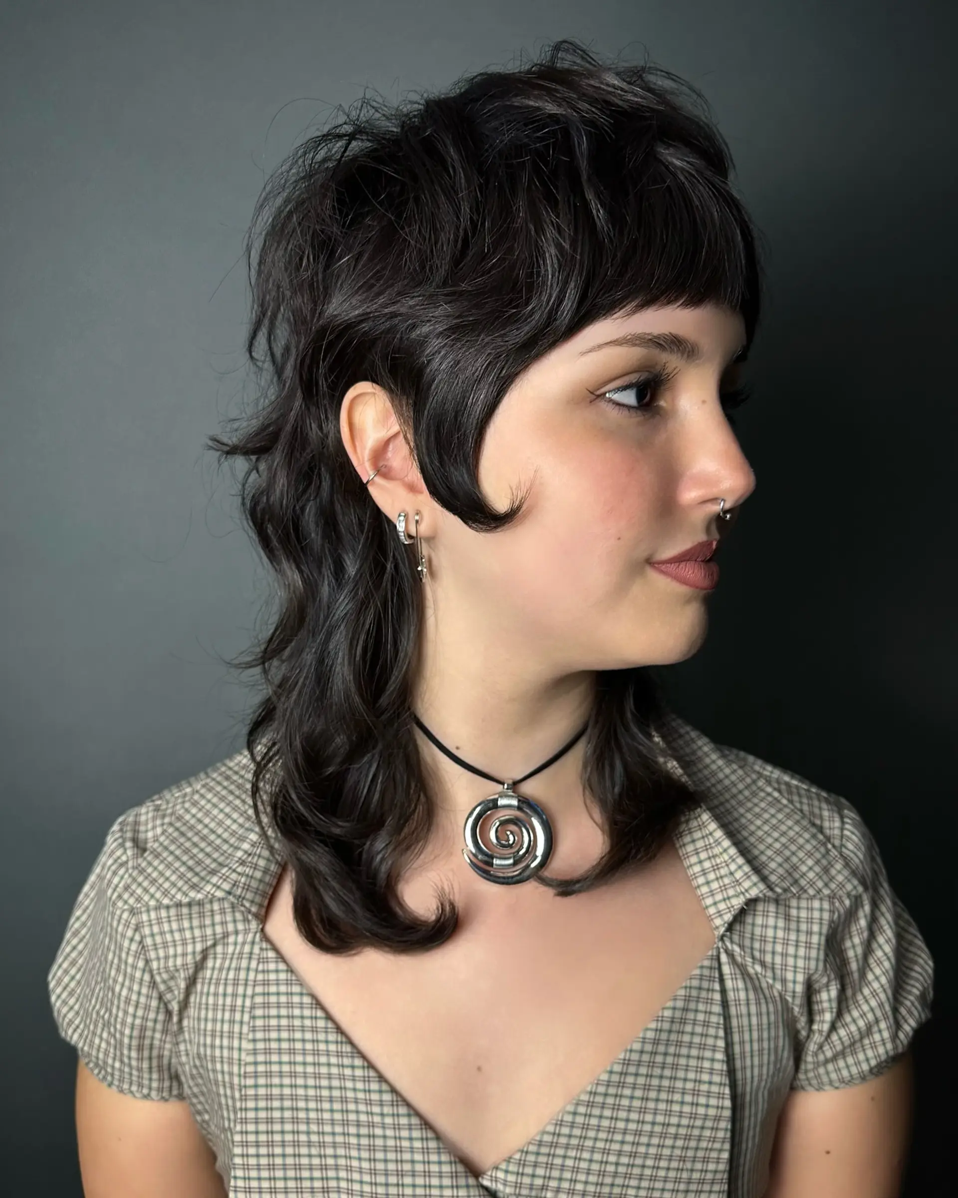 A textured razor cut modern shag mullet featuring blunt micro bangs, flicked cheek-length side pieces, and shoulder-grazing wavy length at the back. 1