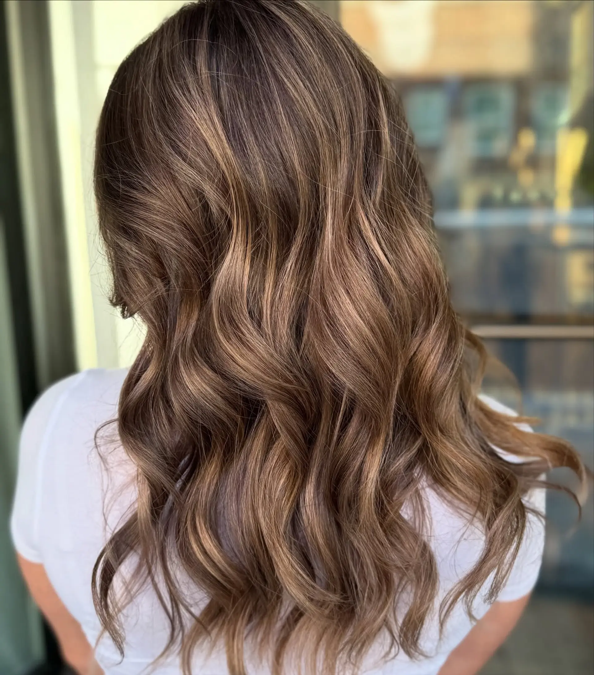 Rich, multi-dimensional warm brunette hair featuring fine, sun-kissed caramel ribbons styled into soft, cascading waves. 1