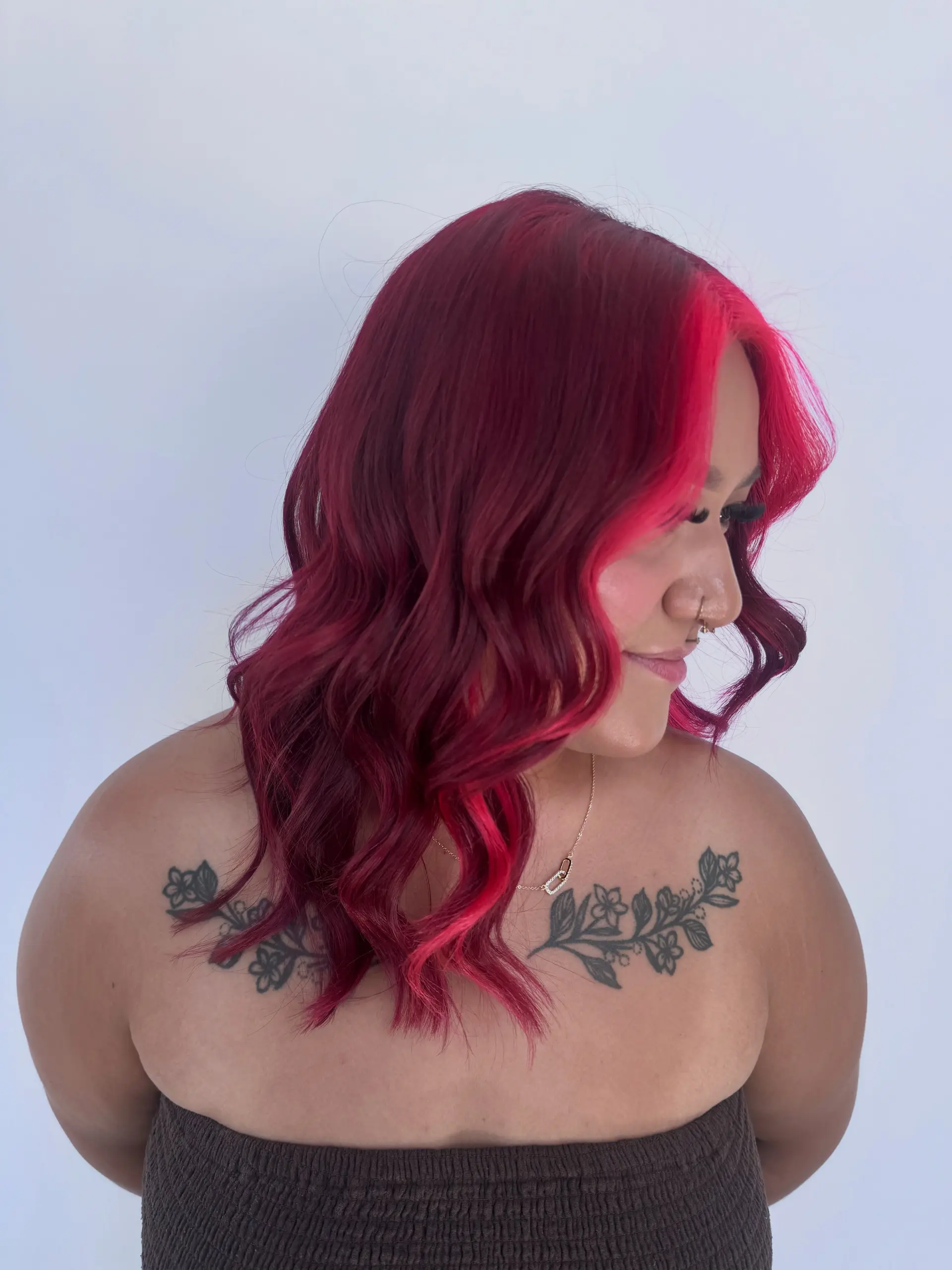 Medium-length wavy crimson red hair styled with a bright, vibrant hot pink face-framing money piece. 1