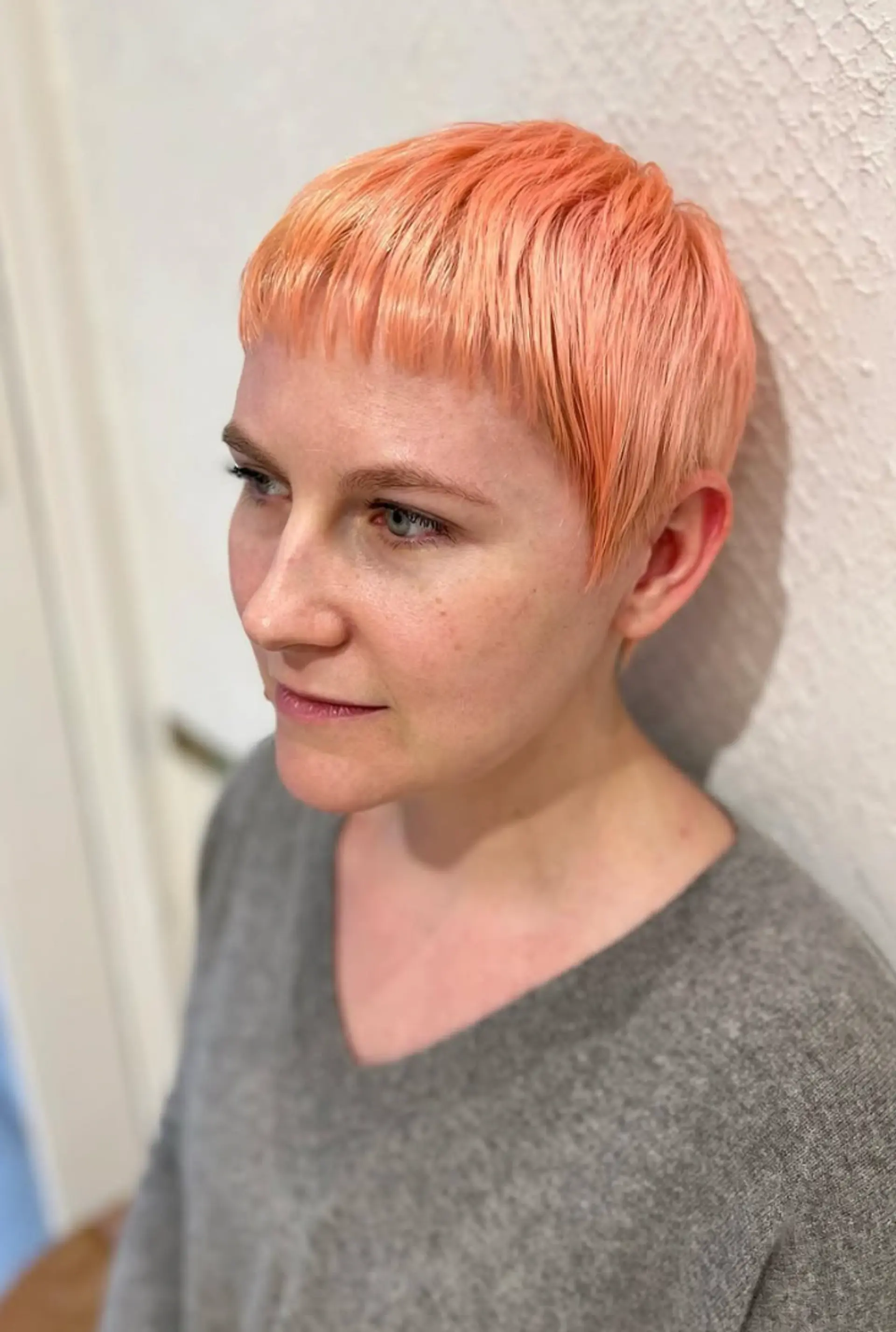 A short, straight pixie cut with choppy layers and a micro fringe, featuring a bold peach and coral color. 1