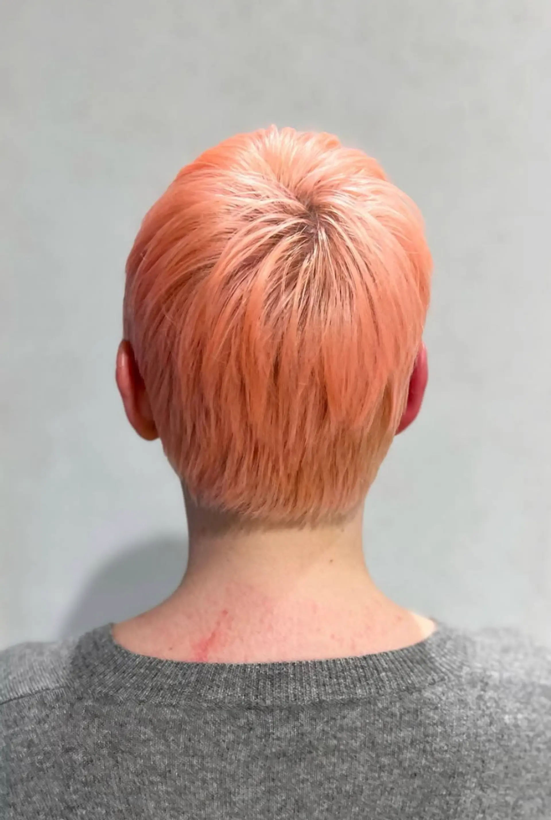 A short, straight pixie cut with choppy layers and a micro fringe, featuring a bold peach and coral color. 2