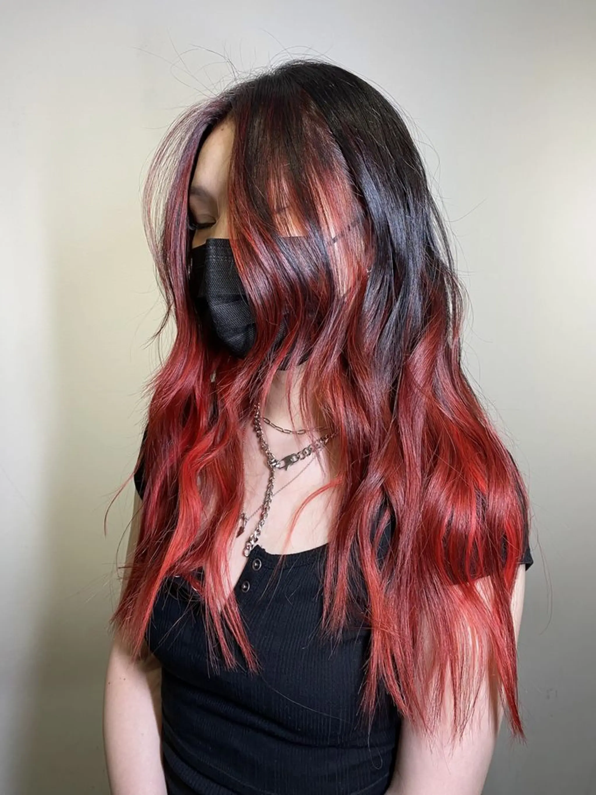 Long, wavy tresses with a black to red ombre effect, featuring subtle layers and soft waves, creating volume and a face-framing, bold look.