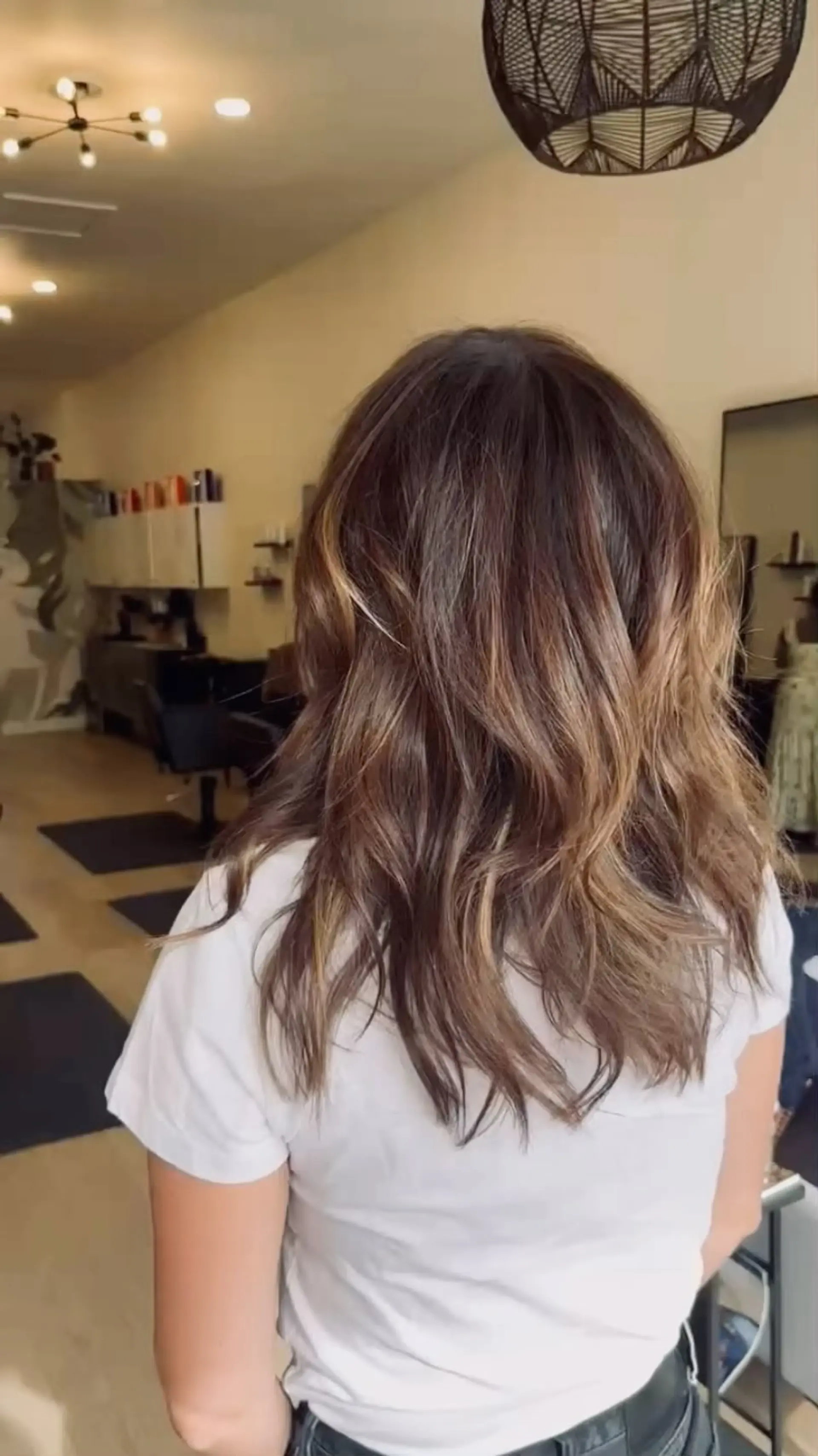 Medium-length layered brunette hair with subtle caramel and honey balayage highlights, styled in loose, soft waves. 1