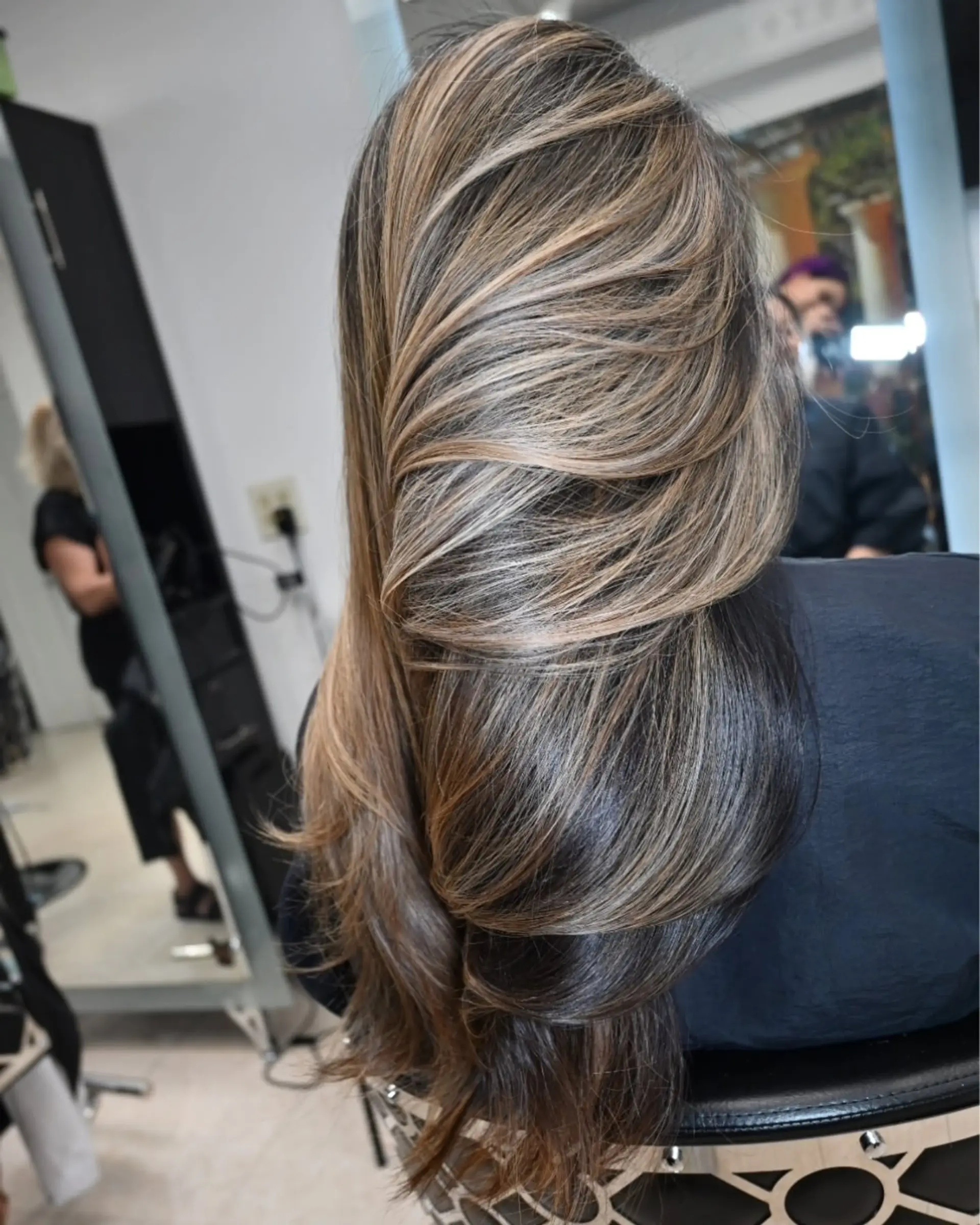 Long dark brown hair enhanced with seamless caramel and honey blonde dimensional highlights, styled into soft, glossy waves. 1