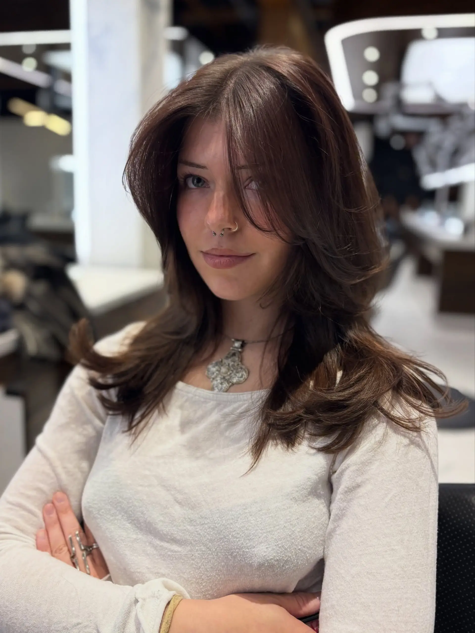 Medium-length chocolate brown hair cut with feathered face-framing layers and curtain bangs, styled into a voluminous blowout with soft outward-flipped ends. 1