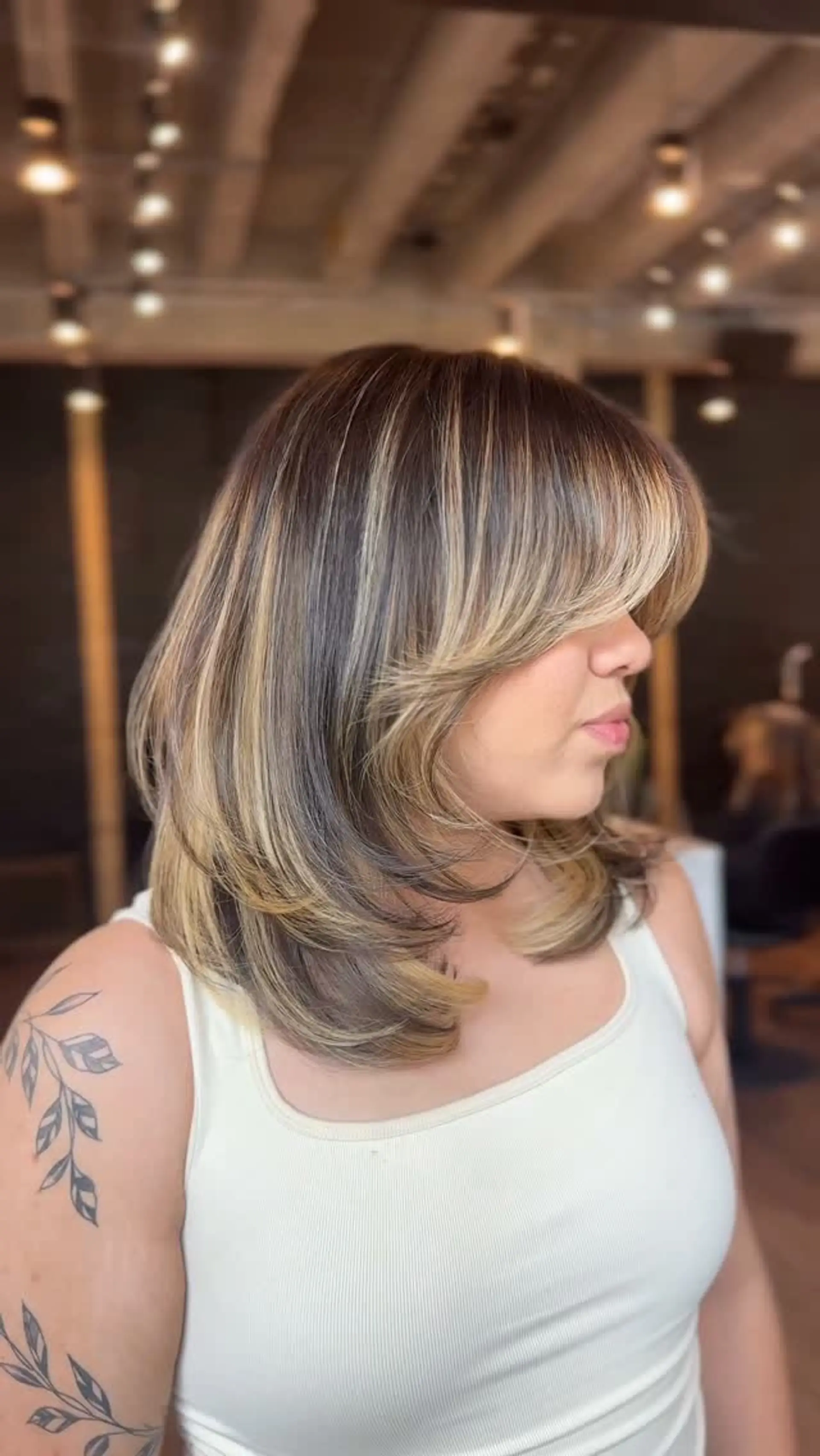A medium-length layered haircut with face-framing curtain bangs styled into a smooth, curved blowout. 1