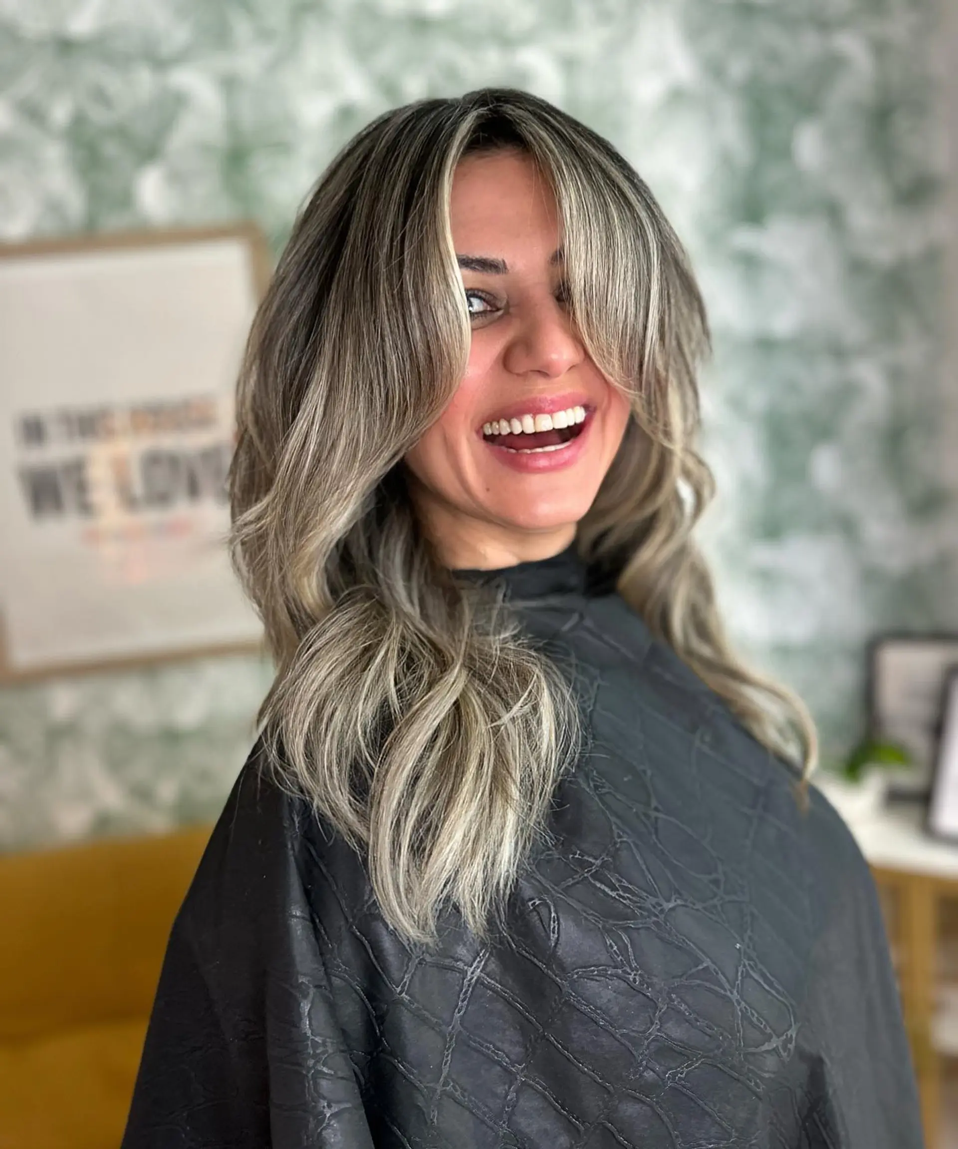 Medium-length textured layered haircut featuring feathered curtain bangs and cool-toned ash blonde highlights. 1