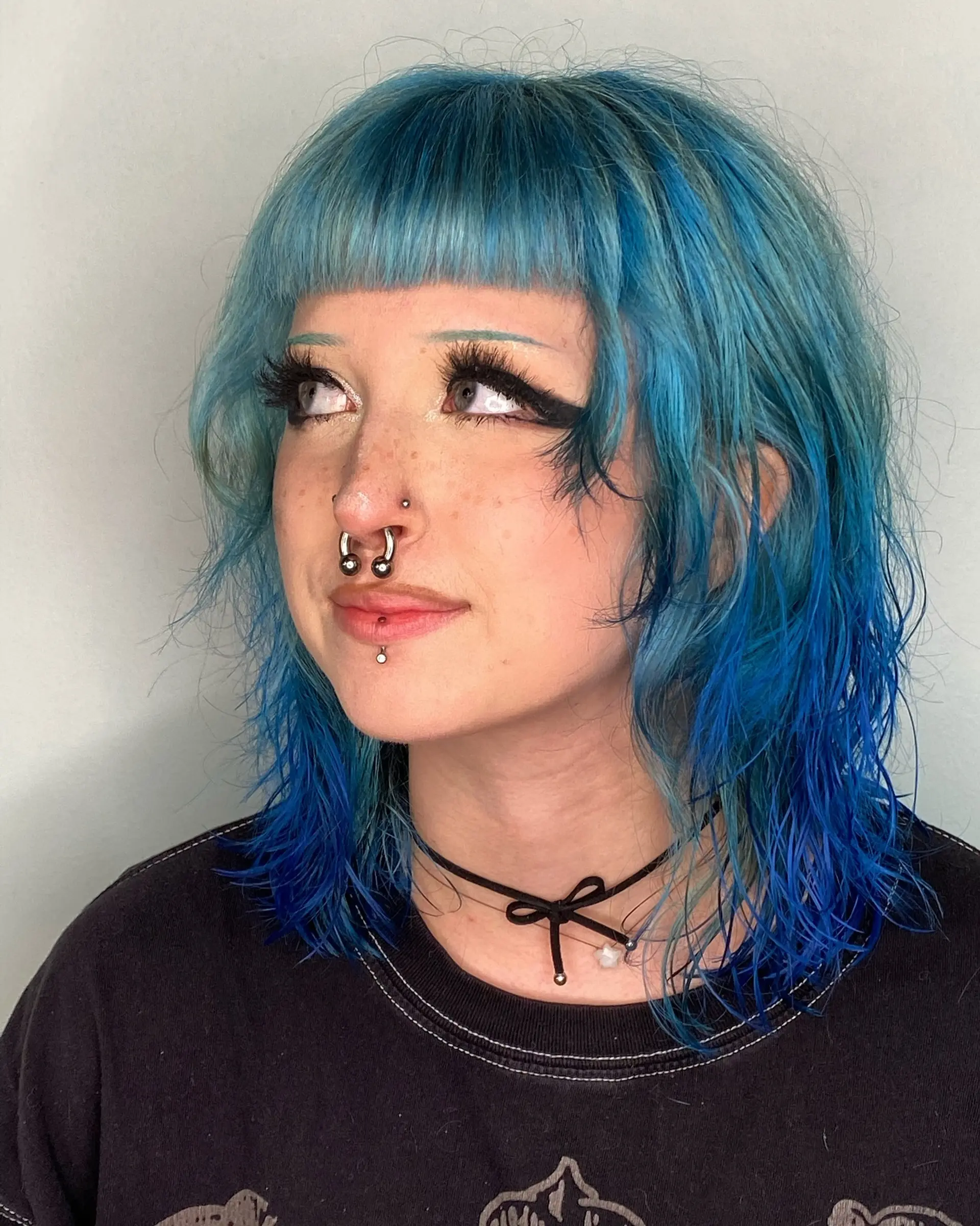 A textured shoulder-length shag haircut with blunt micro baby bangs and face-framing layers, colored in vivid shades of electric blue and teal. 1