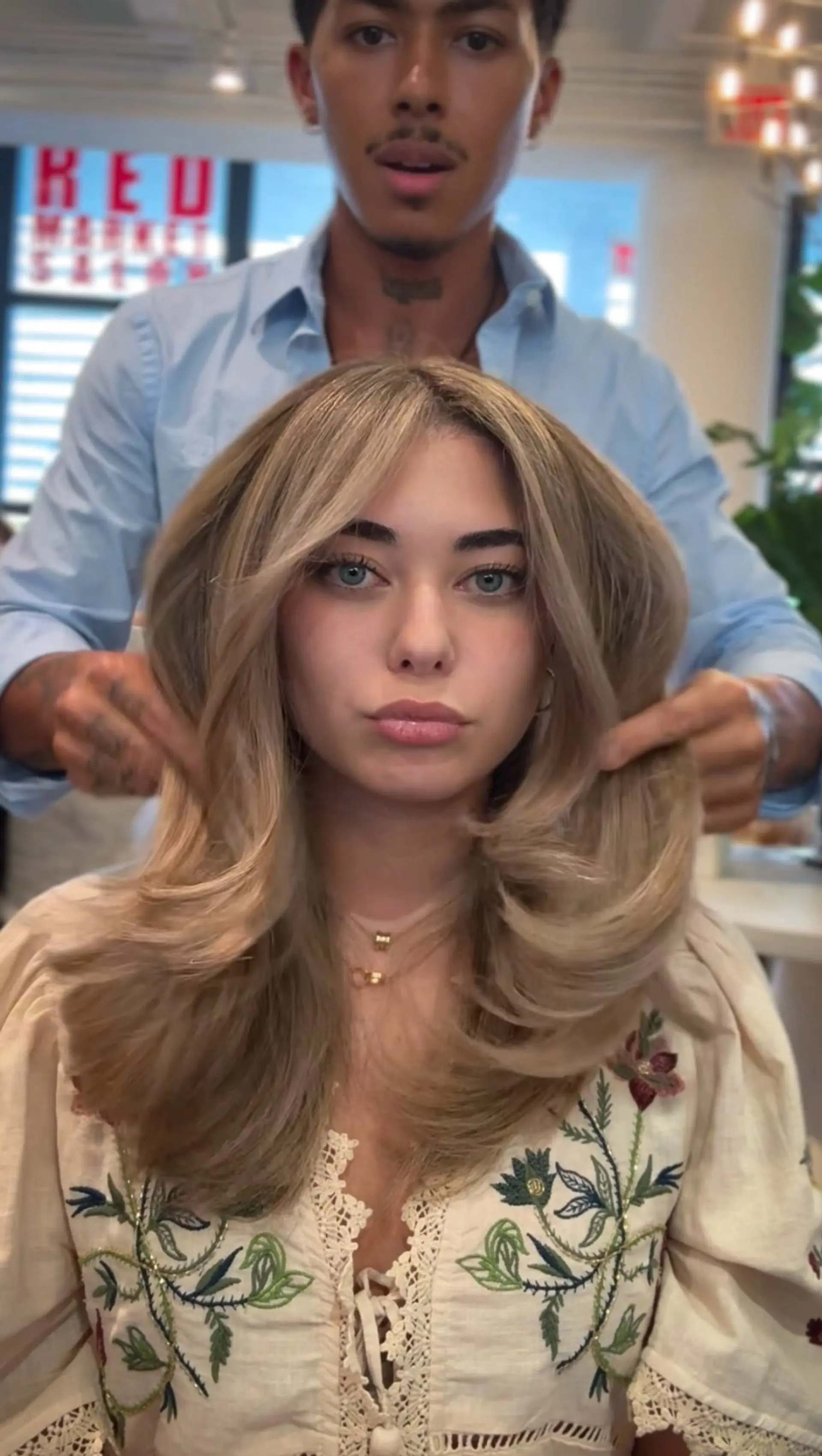 A voluminous blowout featuring soft, feathered face-framing layers and curled-under ends in a seamless neutral blonde shade. 1