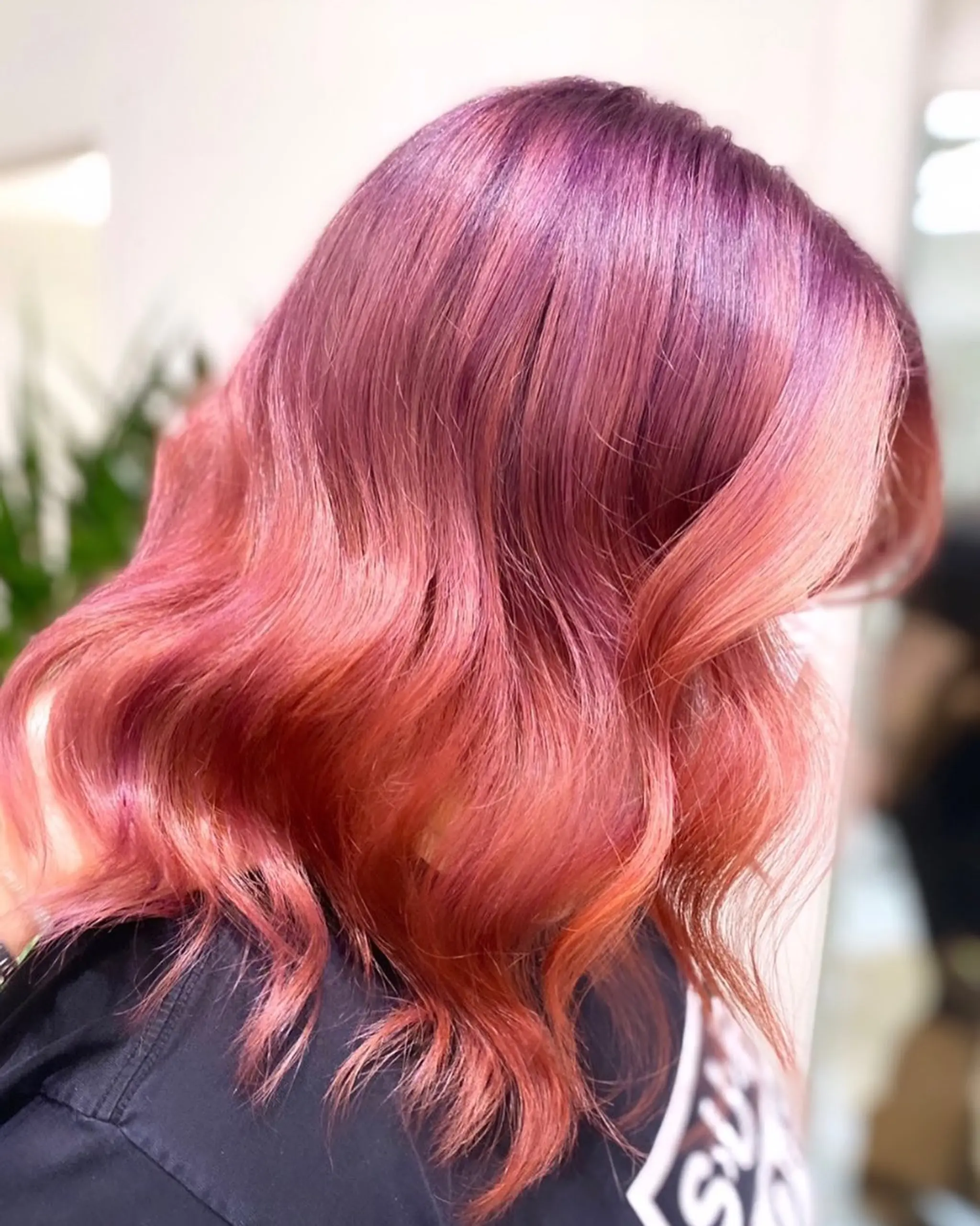 Medium-length, wavy hairstyle with an ombre transition from deep pink to rose gold. Soft, flowing waves add dimension and vibrancy.