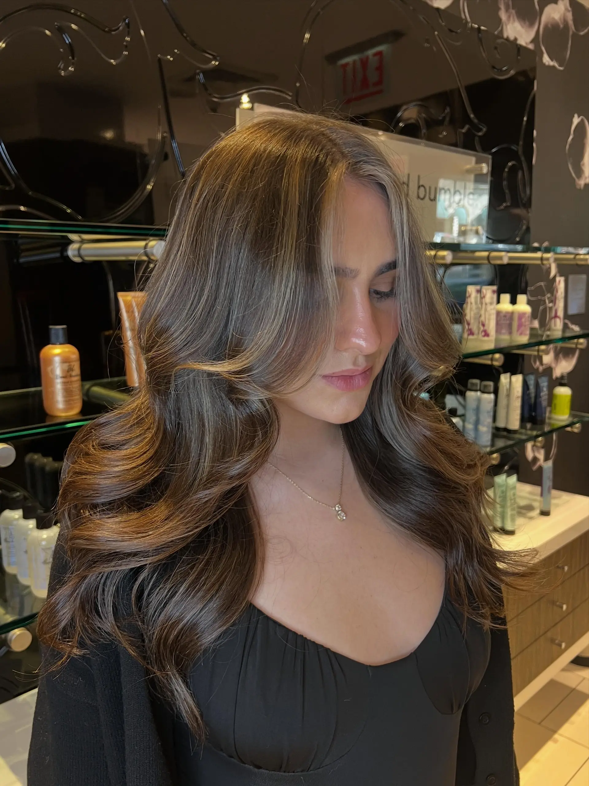 Long dimensional brunette hair styled in a bouncy, voluminous blowout featuring subtle balayage and bright face-framing tendrils. 1