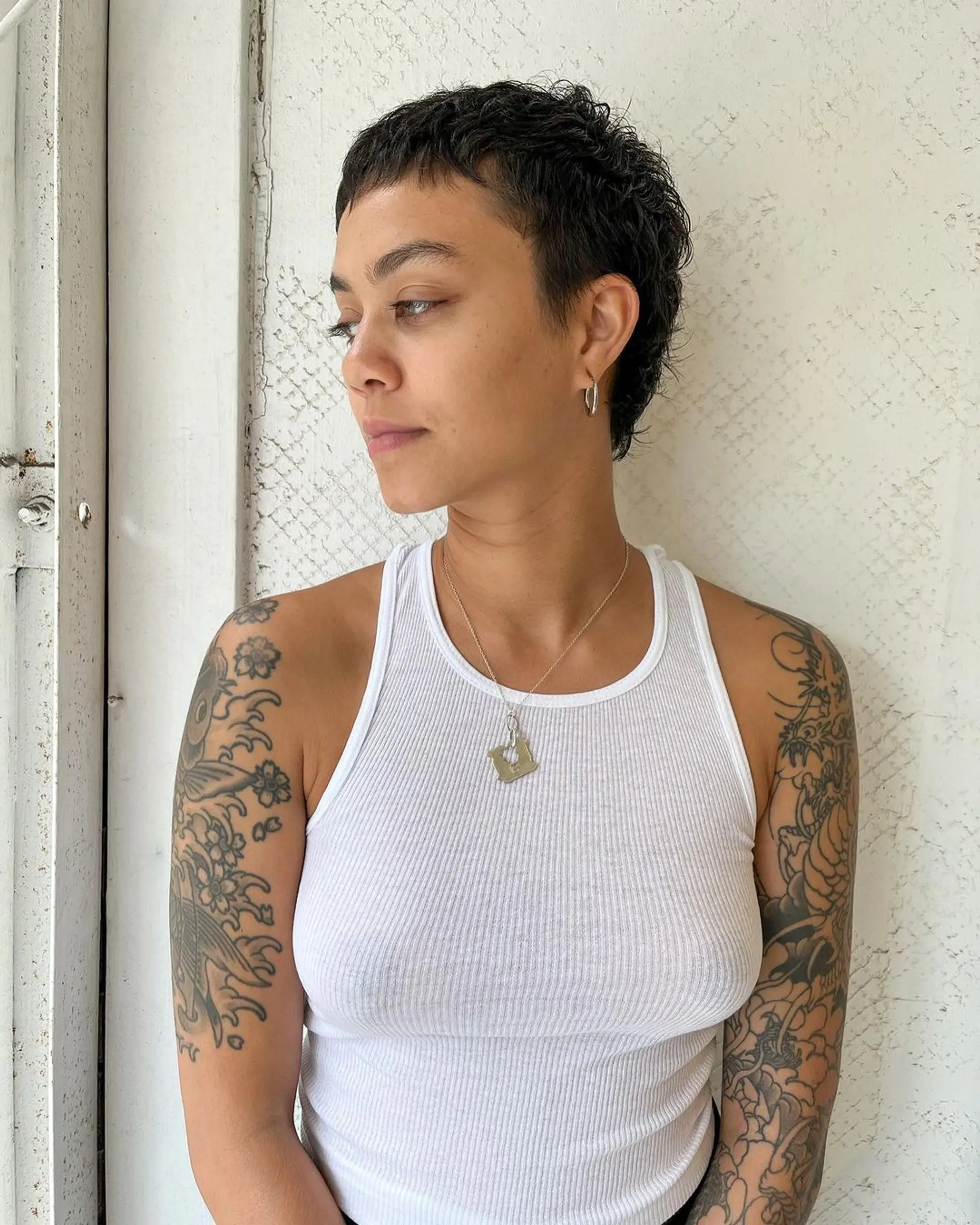 Short, naturally wavy hair styled into an edgy pixie cut with textured waves and a subtle fringe. 1