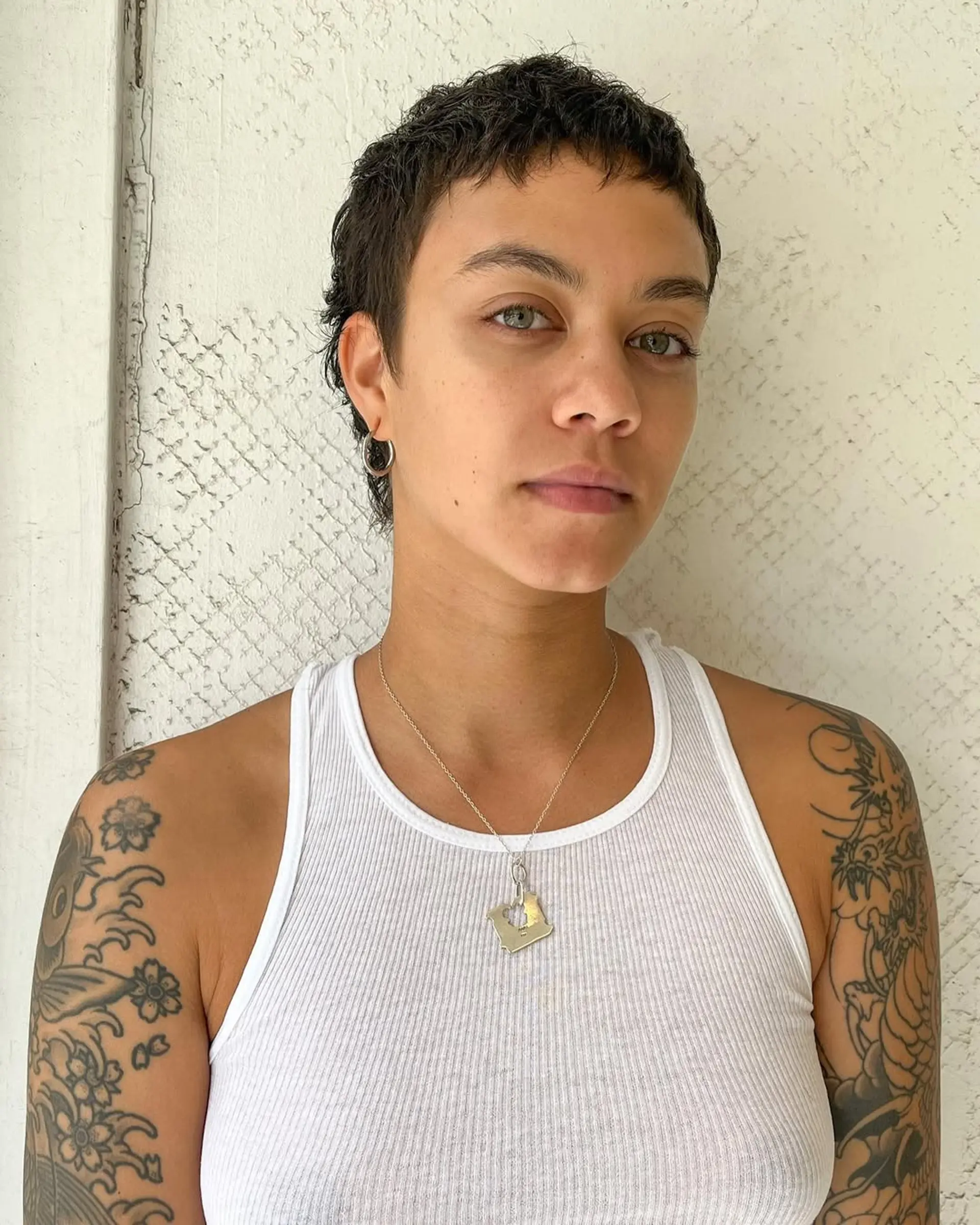 Short, naturally wavy hair styled into an edgy pixie cut with textured waves and a subtle fringe. 2