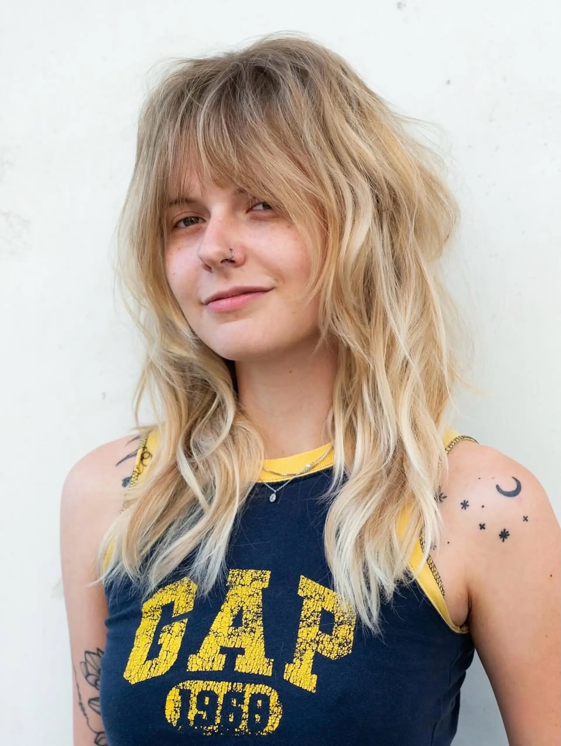Medium-length blonde shag haircut with choppy layers, soft full bangs, and effortless wave texture. 1