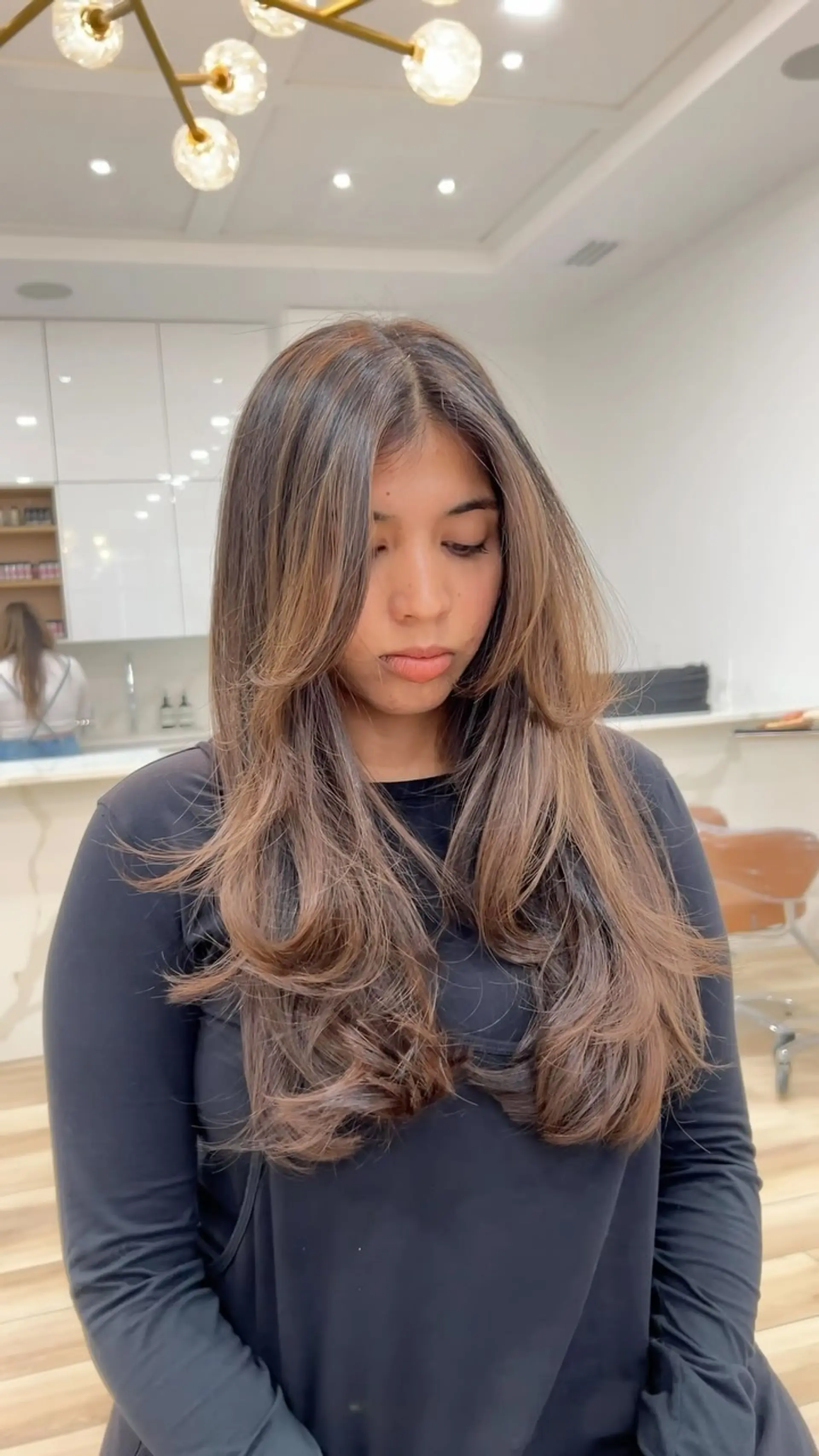 Long dimensional brunette hair styled with voluminous layers, face-framing curtain bangs, and soft curled ends. 1