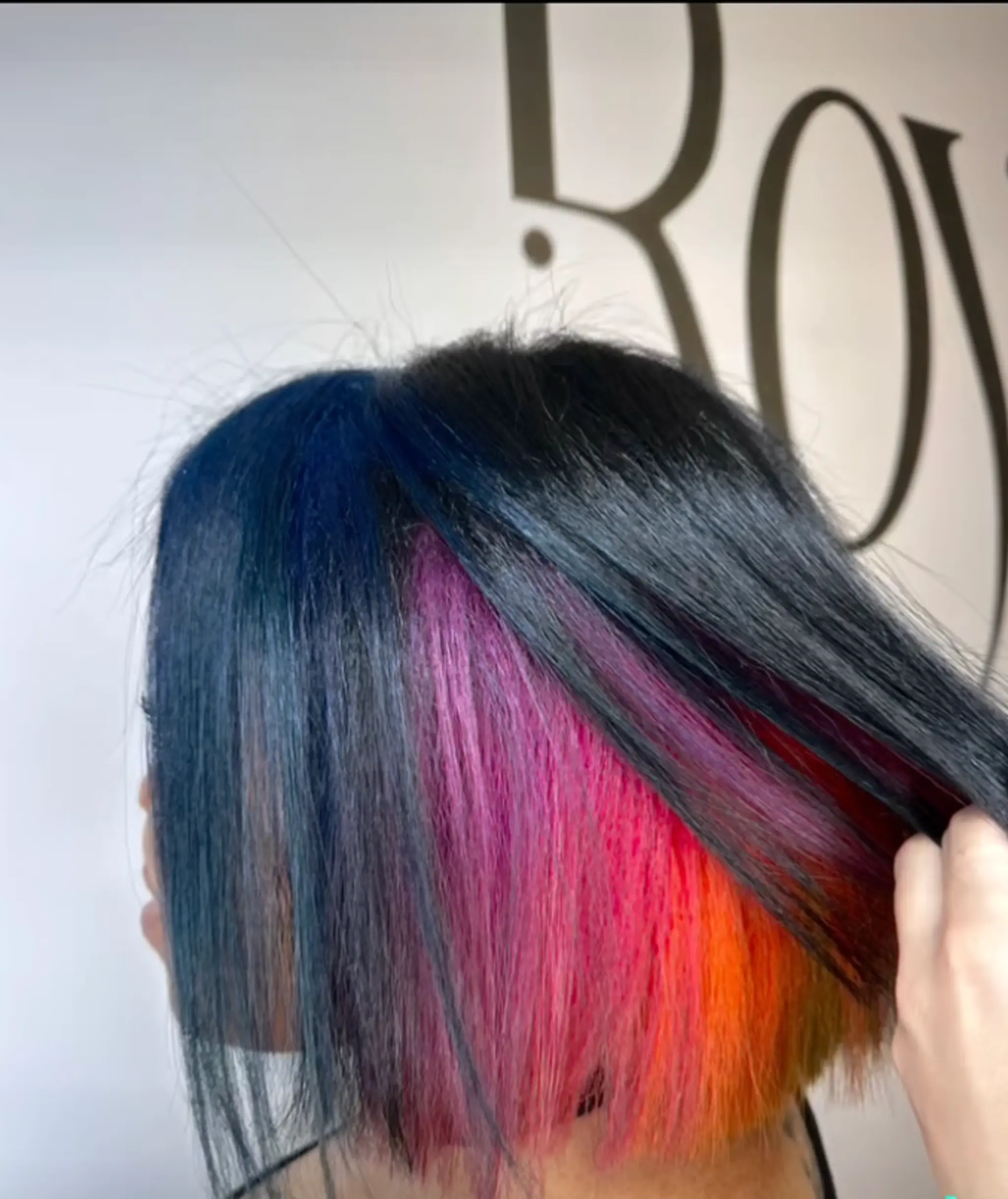 Asymmetrical bob with black roots transitioning into blue, pink, and orange highlights. Medium length with a sleek, straight texture.

Color by @simabeautynyc
Cut and style by @juliamannino_hair
