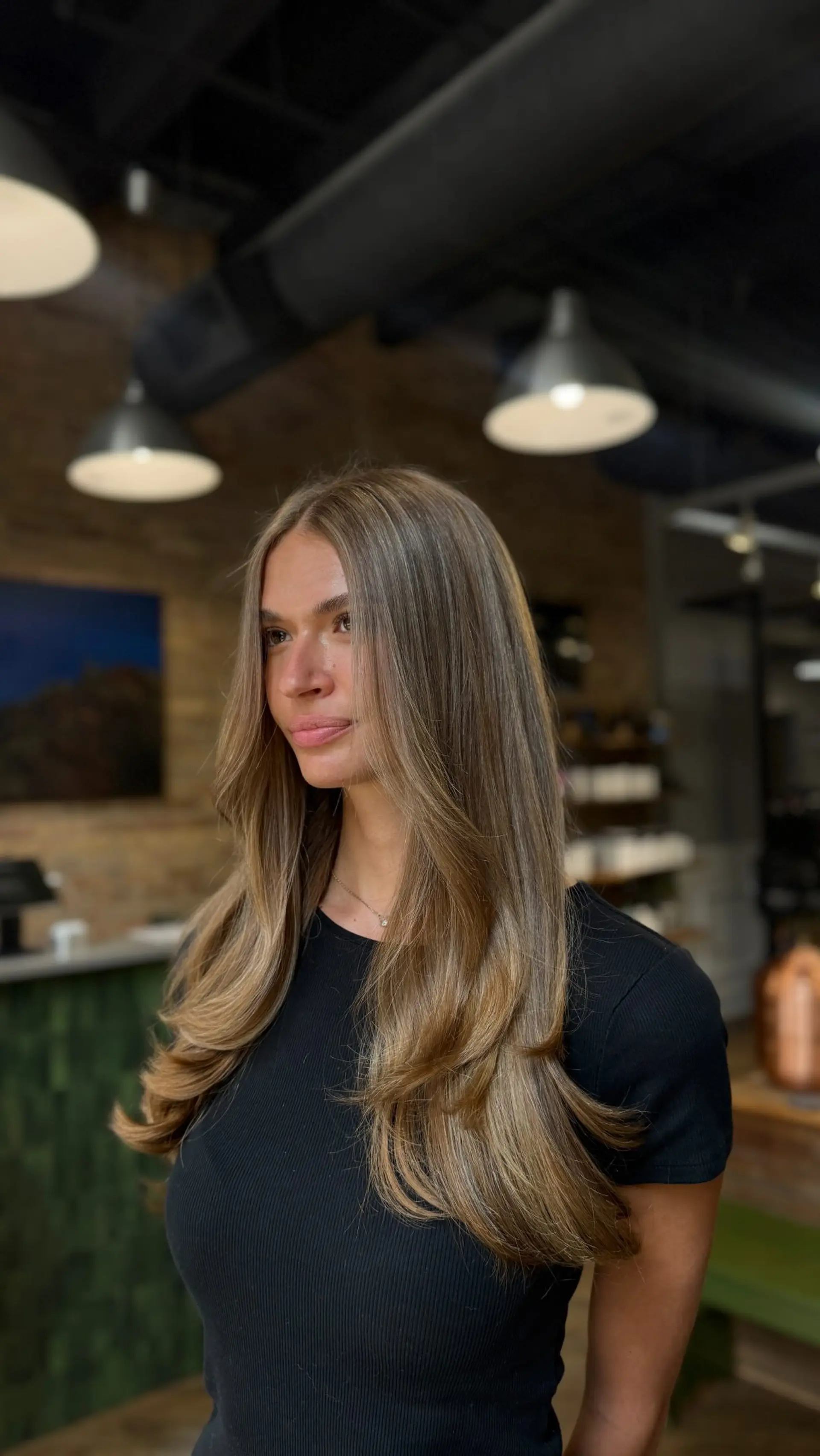 Long bronde hair cut with soft face-framing layers and styled into a voluminous blowout with flipped-in ends. 1