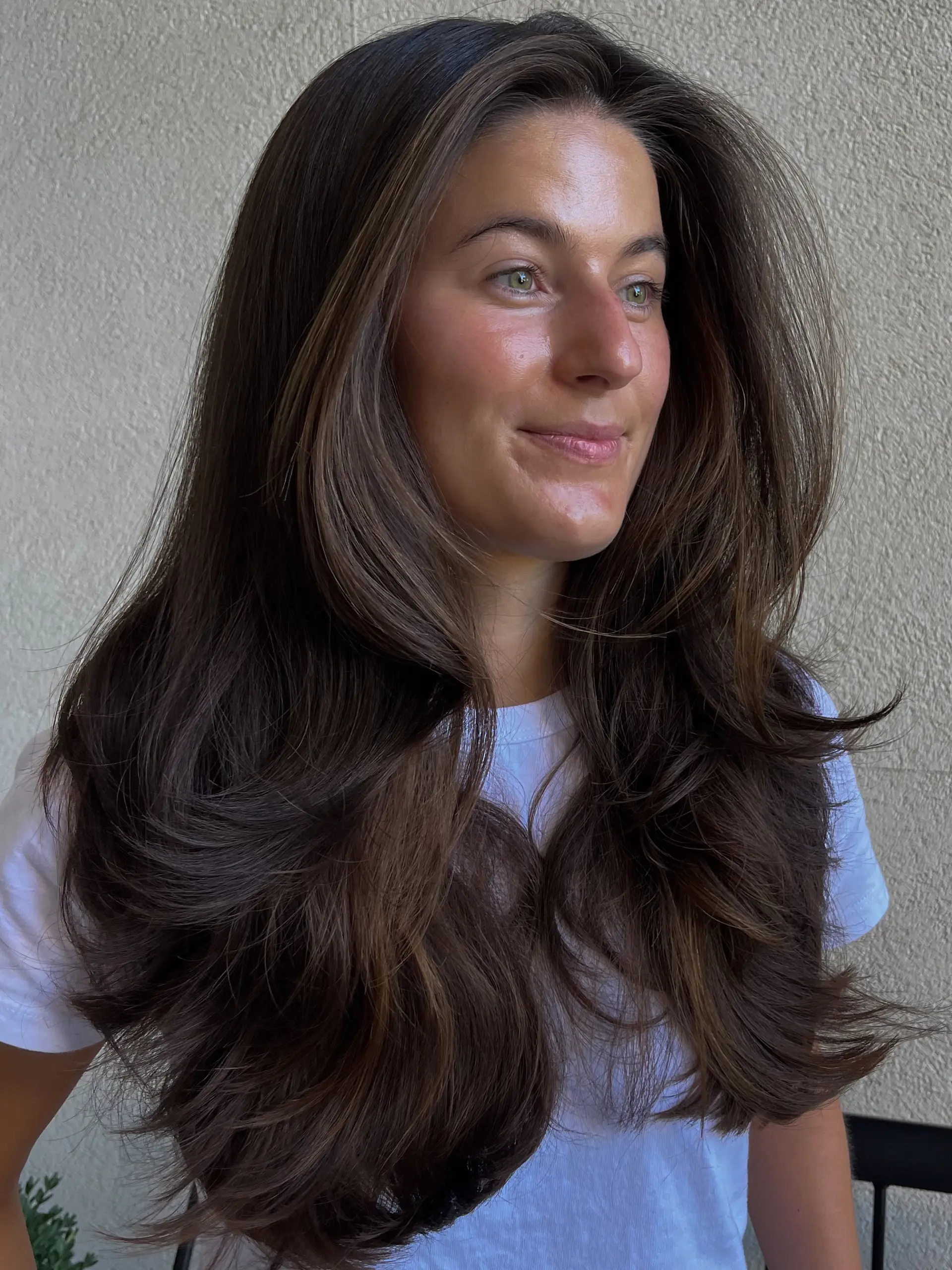 Long brunette hair cut with bouncy layers and soft face-framing details, styled into a voluminous blowout. 1
