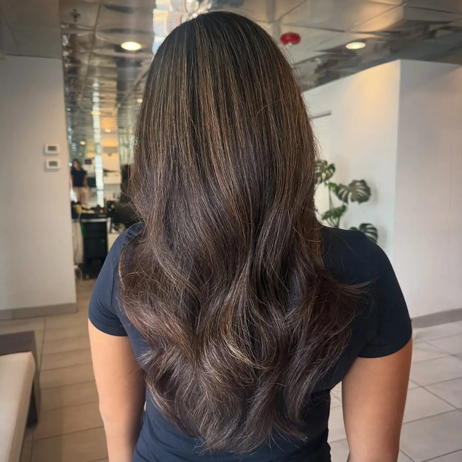 Long layered brunette hair featuring a seamless, subtle balayage with soft blowout waves at the ends. 1