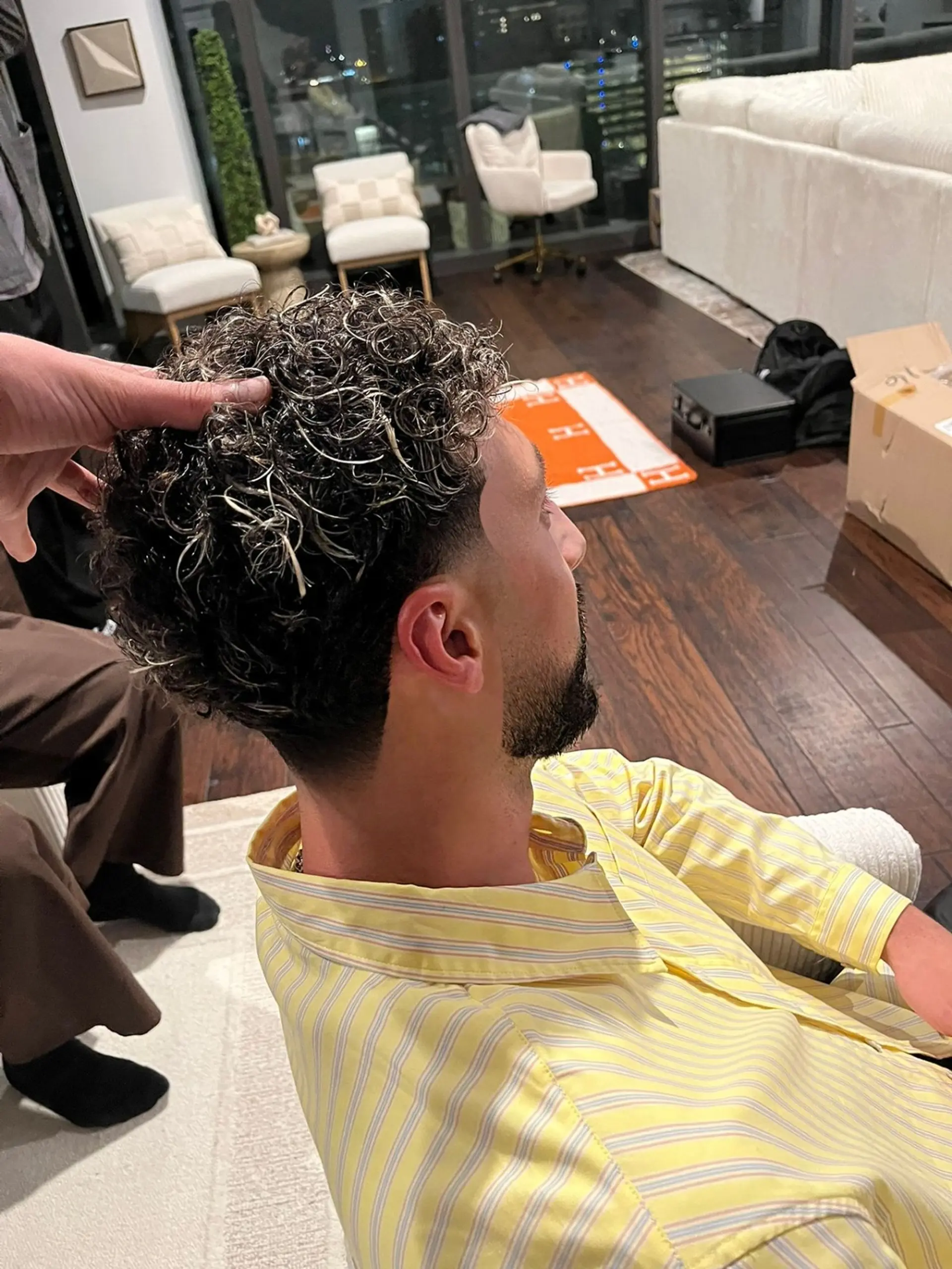 A men's short haircut featuring defined curly texture with blonde tips on top, complemented by a low taper fade and a crisp beard lineup. 1