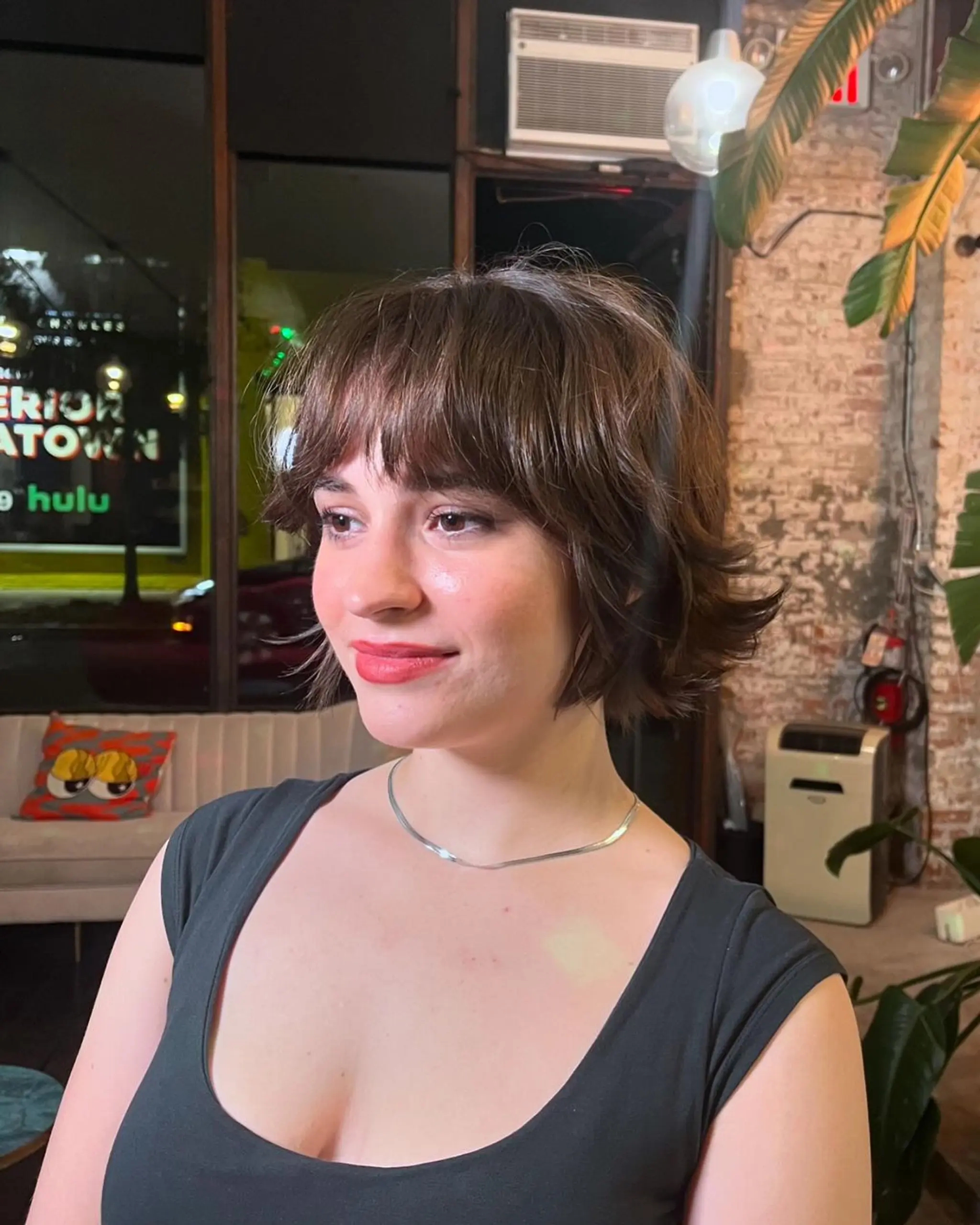 A chic, short, wavy hairstyle with chestnut brown hair styled into a textured bob featuring playful waves and a feathered fringe. The style offers a casual elegance with its subtle volume and tousled appearance. 2
