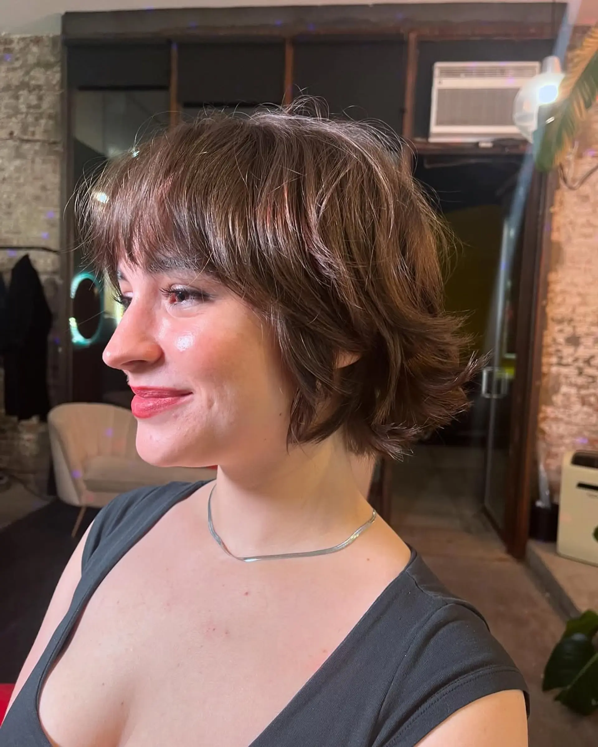 A chic, short, wavy hairstyle with chestnut brown hair styled into a textured bob featuring playful waves and a feathered fringe. The style offers a casual elegance with its subtle volume and tousled appearance. 1