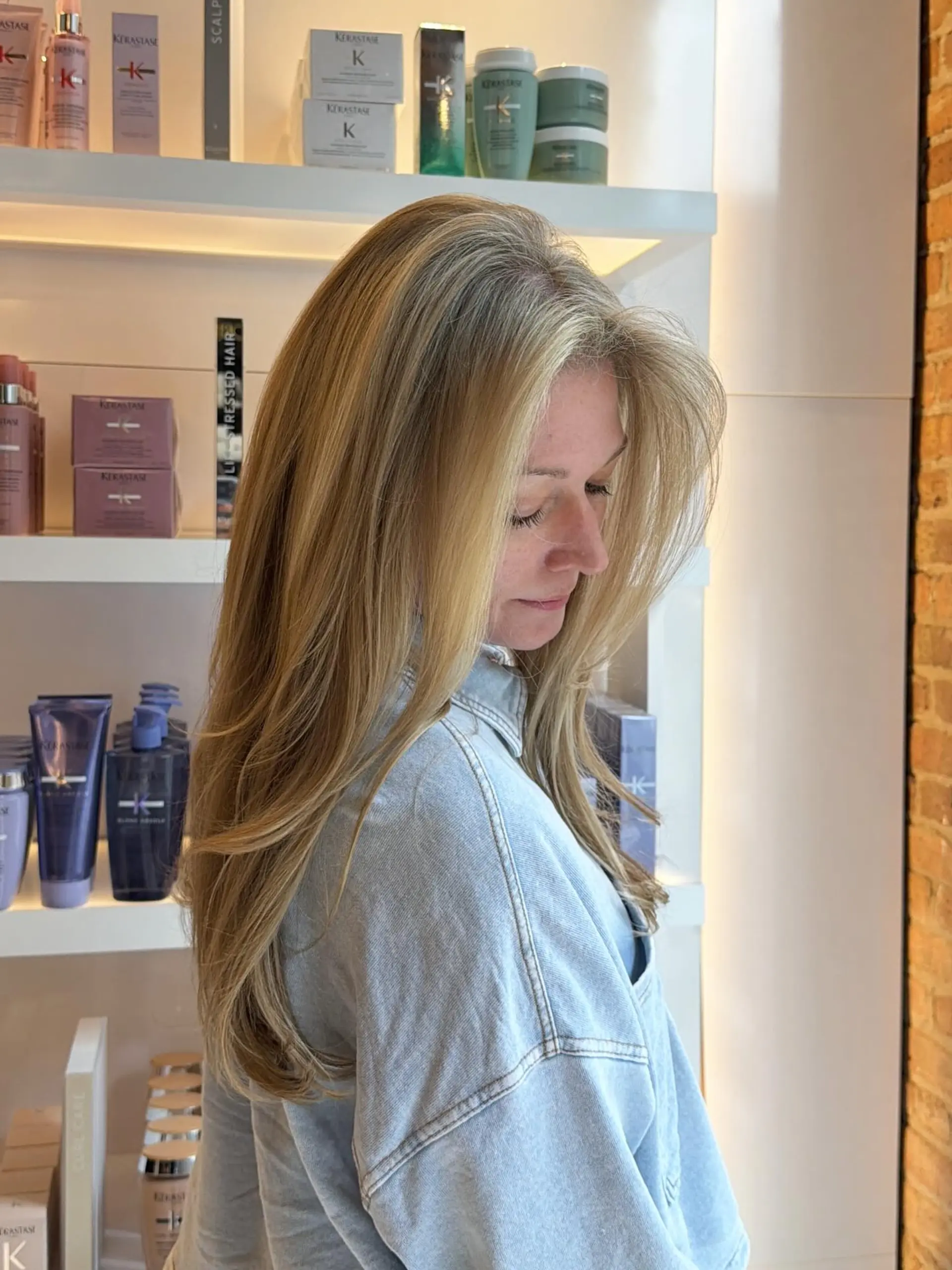 Long layered blonde hair styled in a smooth, voluminous blowout with feathered, face-framing layers. 1