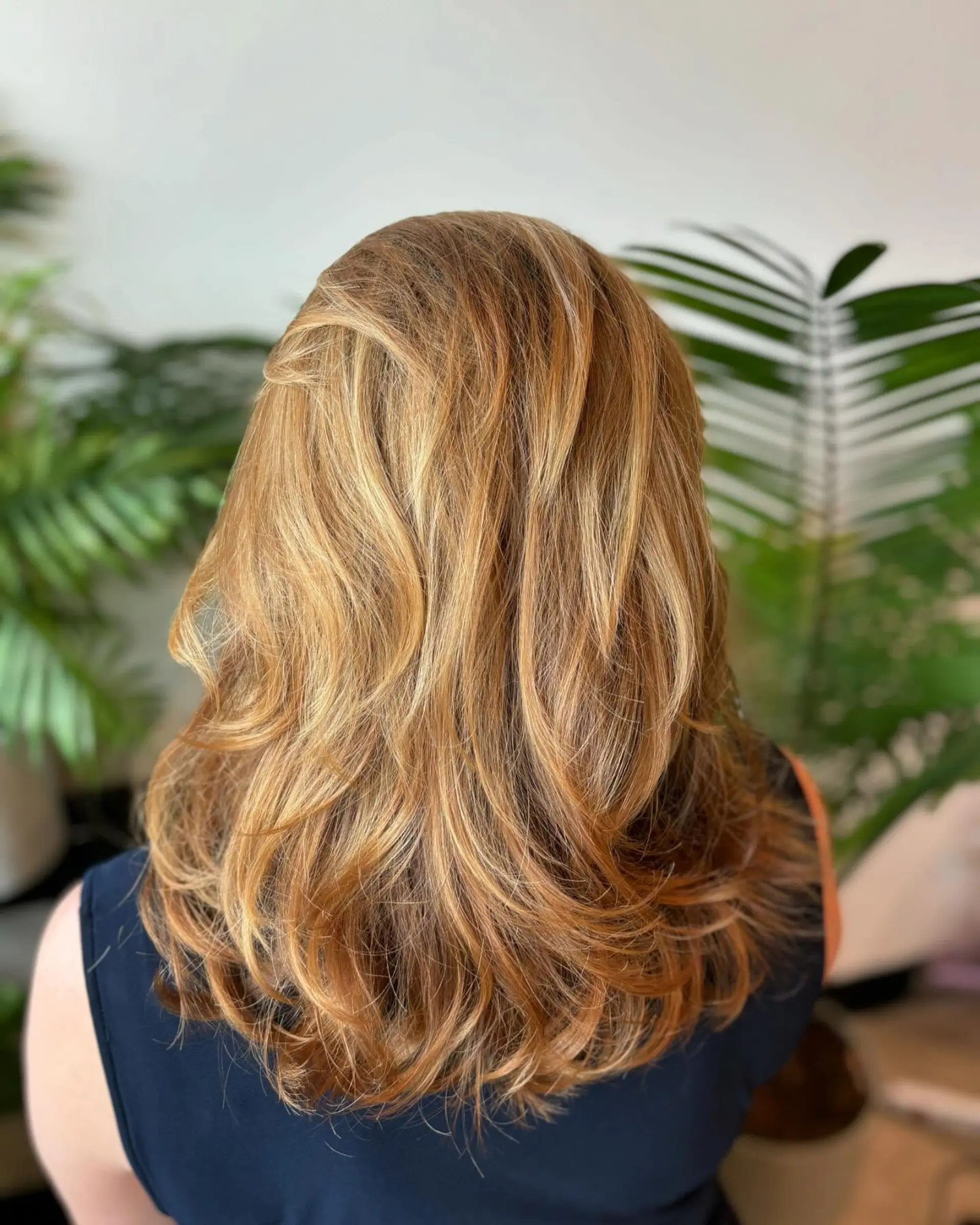 Medium-length layered cut styled with soft curved waves and warm golden blonde balayage highlights. 1
