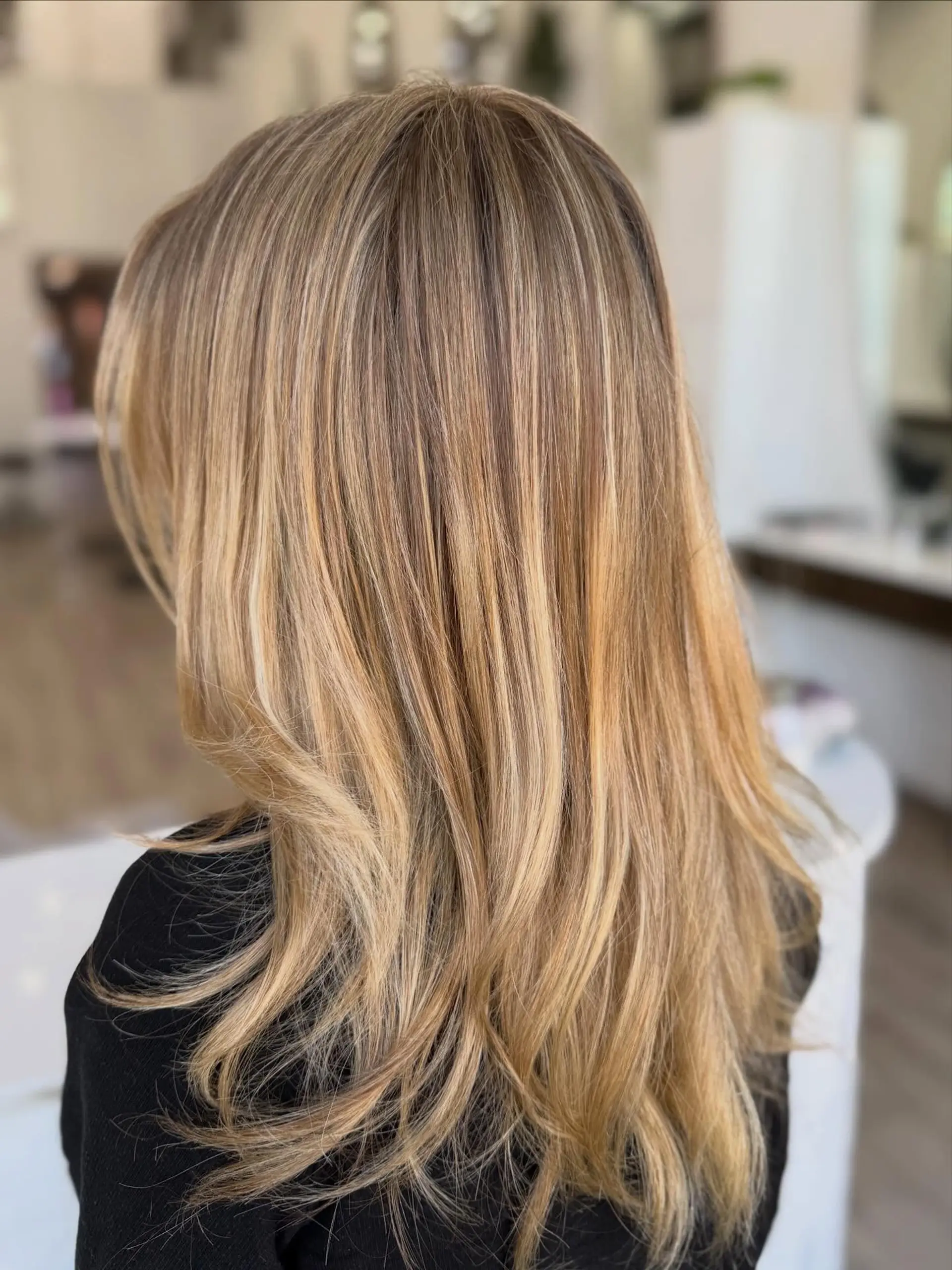 Long layered hair featuring seamless golden blonde highlights blended into a warm light brown base, finished with a smooth blowout. 1