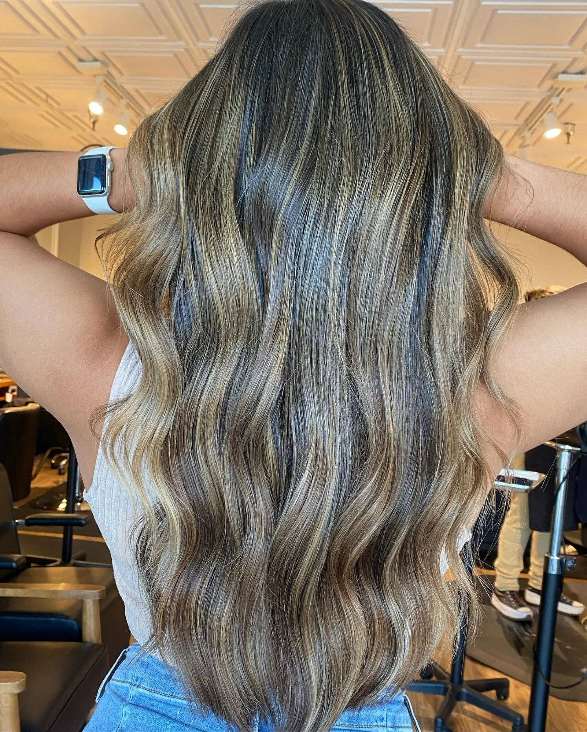 Long cascading hair featuring multidimensional warm blonde and caramel highlights blended over a deep brunette base, styled with soft, voluminous waves. 1