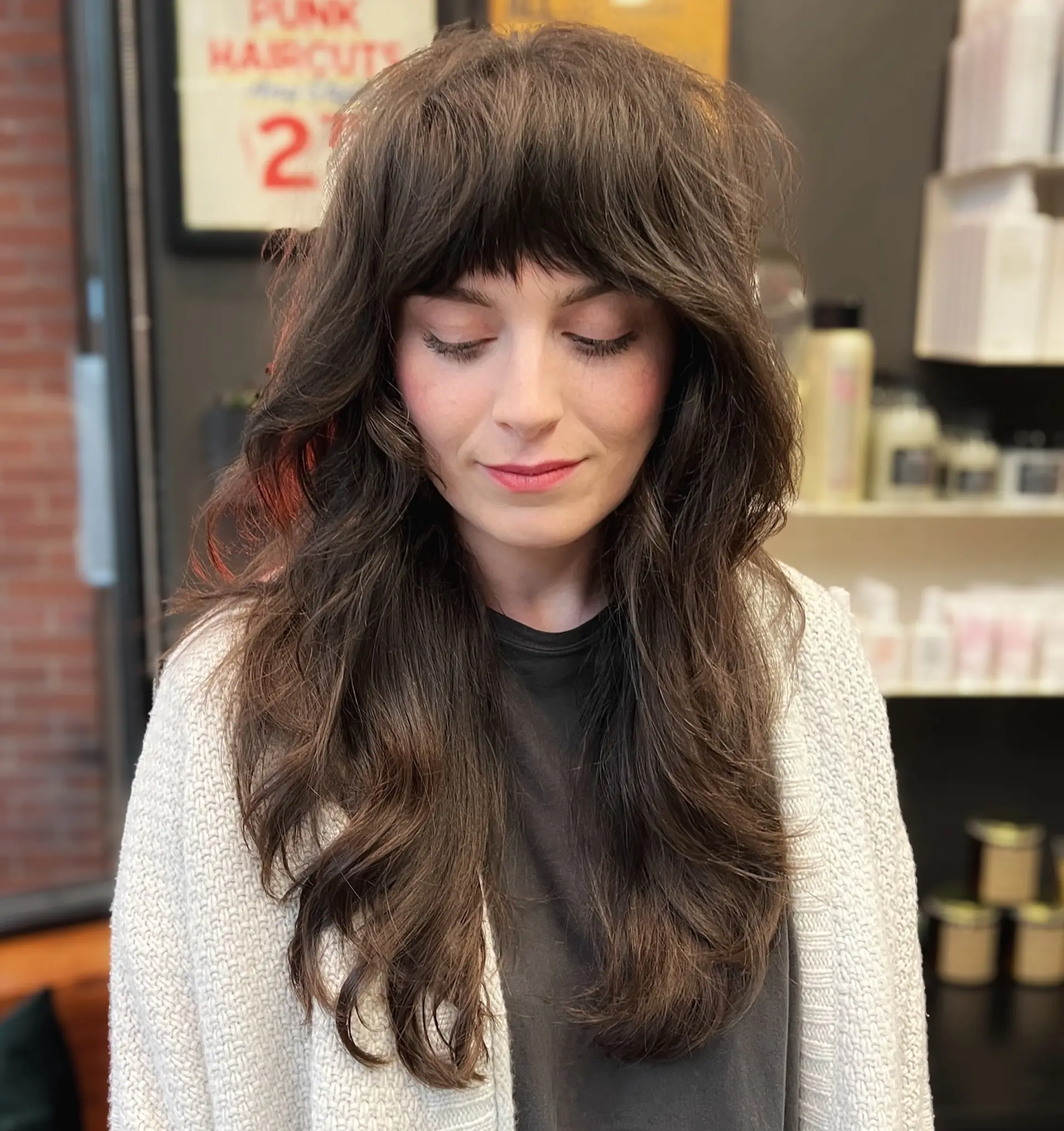 A long, textured brunette shag haircut featuring full piecey fringe bangs and layered face-framing waves. 1