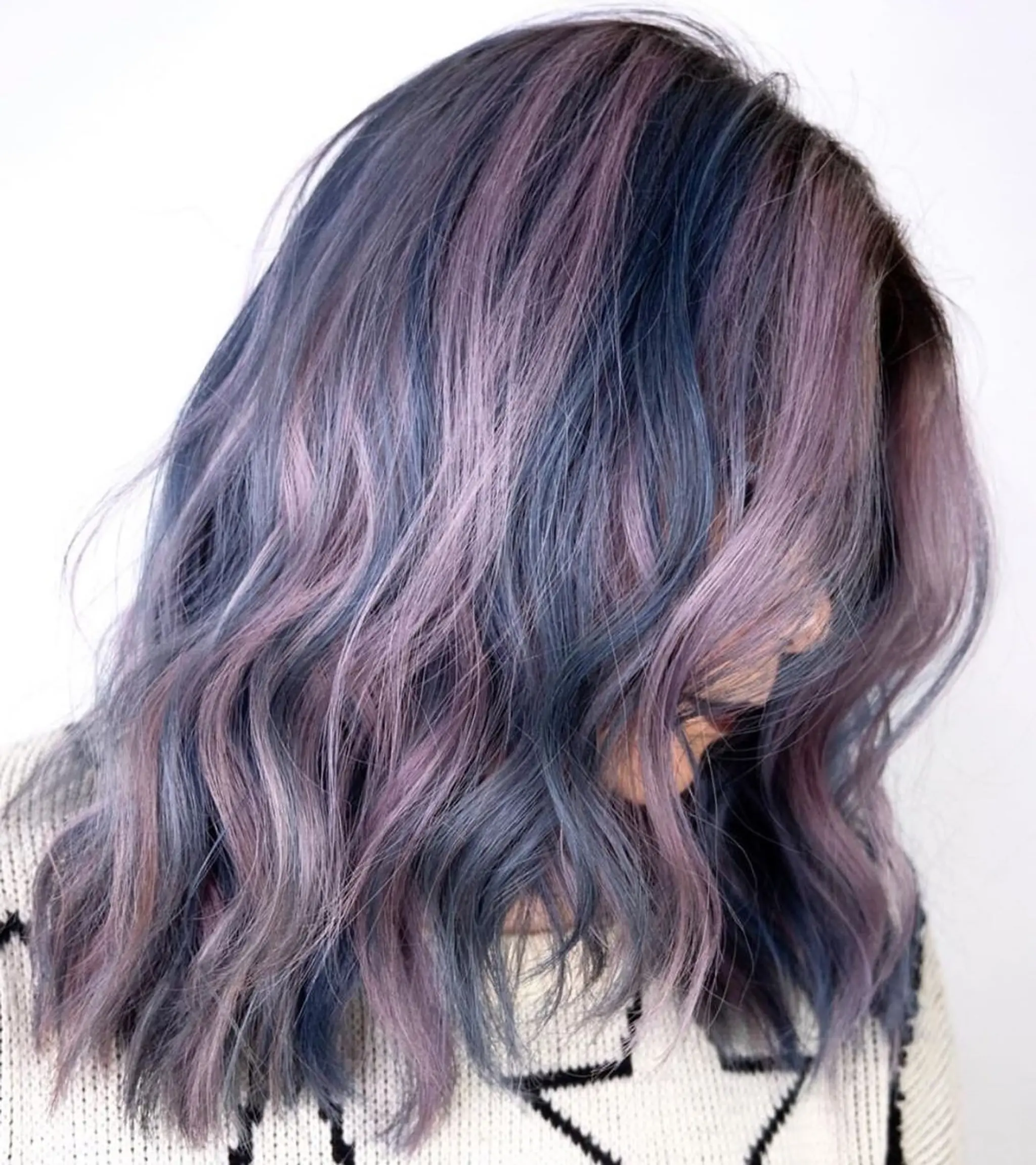 A medium-length wavy hairstyle featuring a blend of purple, blue, and gray hues. The colors transition seamlessly, creating a dreamy, iridescent effect. Soft waves add volume and texture, giving the hairstyle a relaxed yet sophisticated appearance.