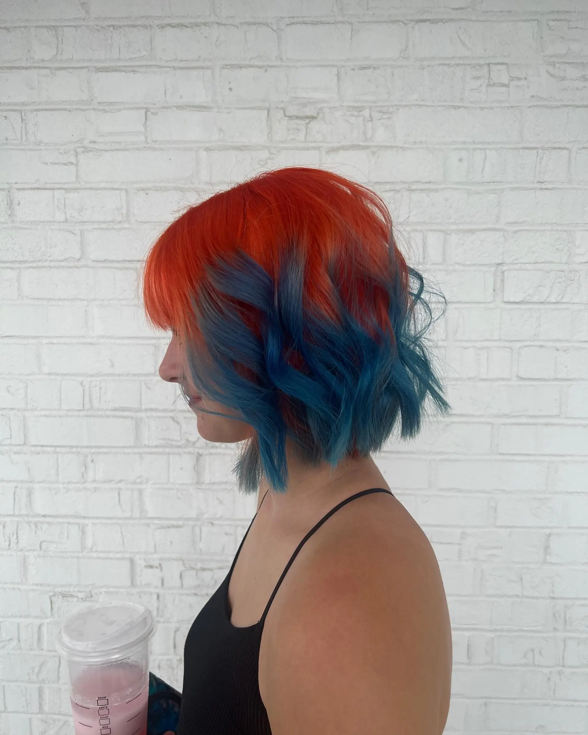 A textured chin-length wavy bob cut featuring an electric two-tone color design with bright orange at the crown fading into rich vivid blue ends. 1