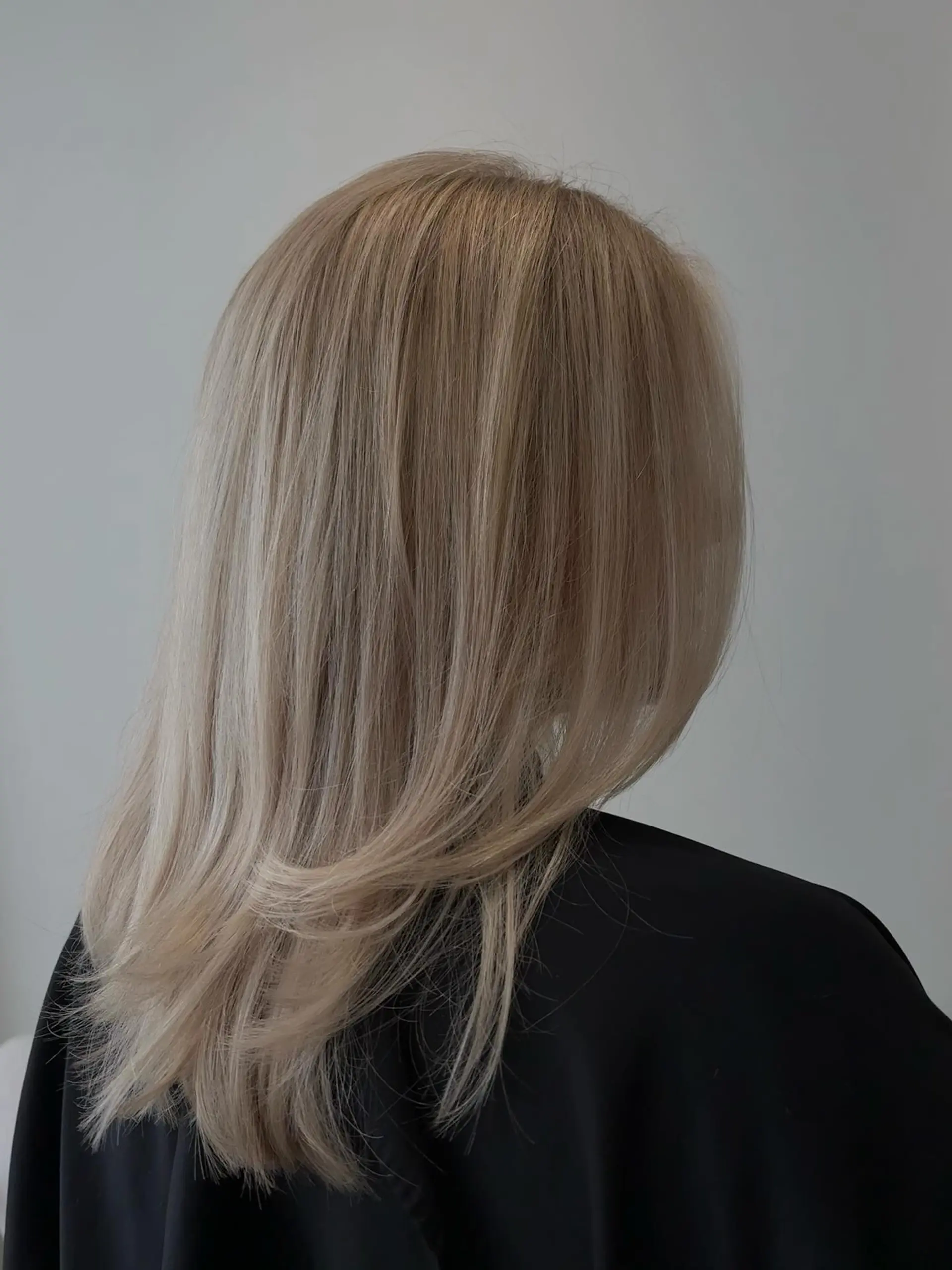 Silky ash blonde hair styled straight with soft, inward-turned layered ends. 1