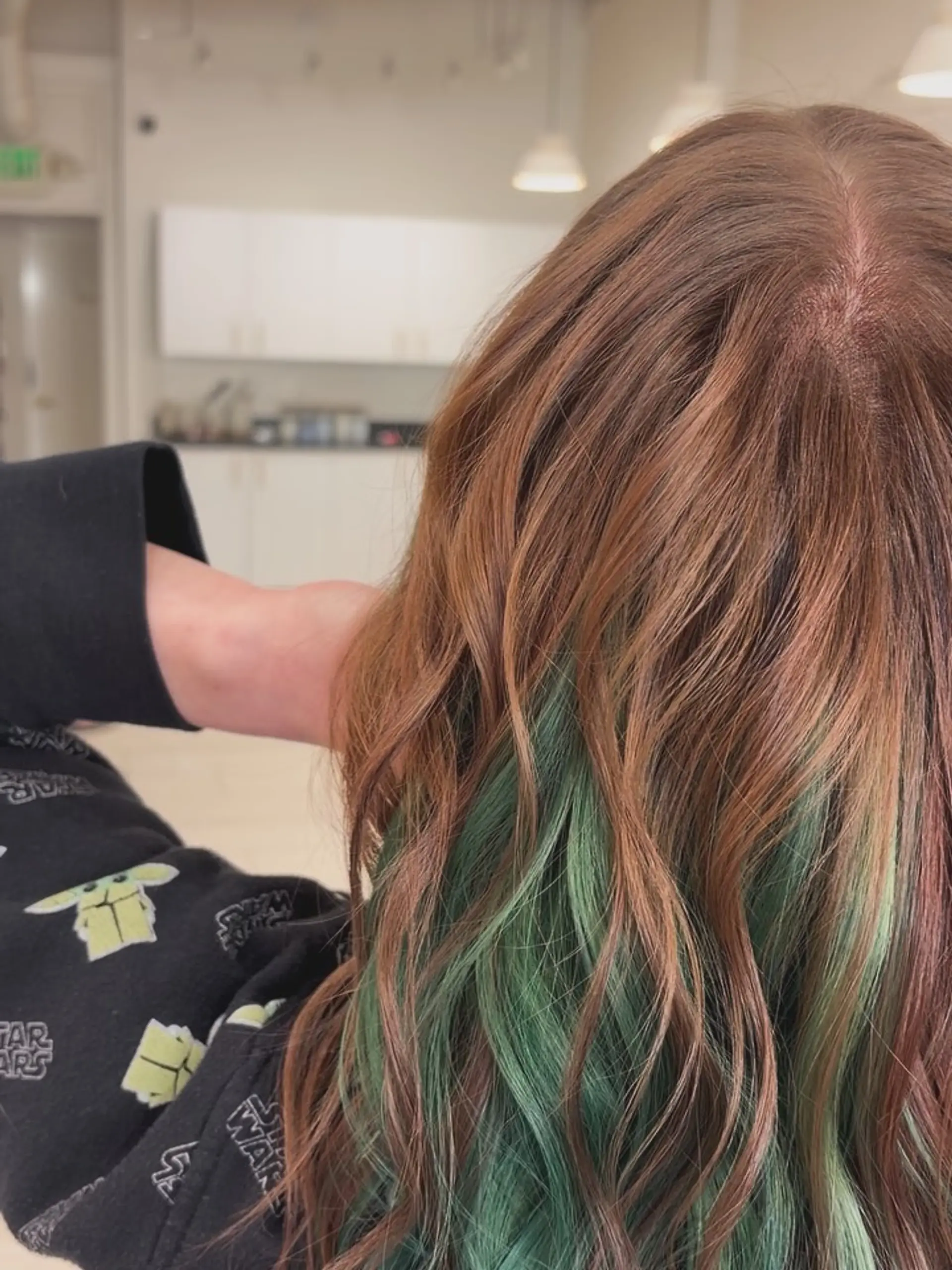 Medium-length warm brown hair styled in soft waves with a vibrant green peekaboo underlayer. 1