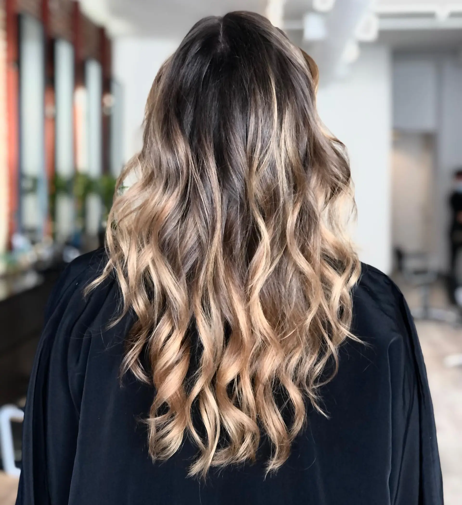 Long lived-in balayage transitioning from a natural brunette base into dimensional honey-blonde ribbons, styled in loose, beachy waves. 1