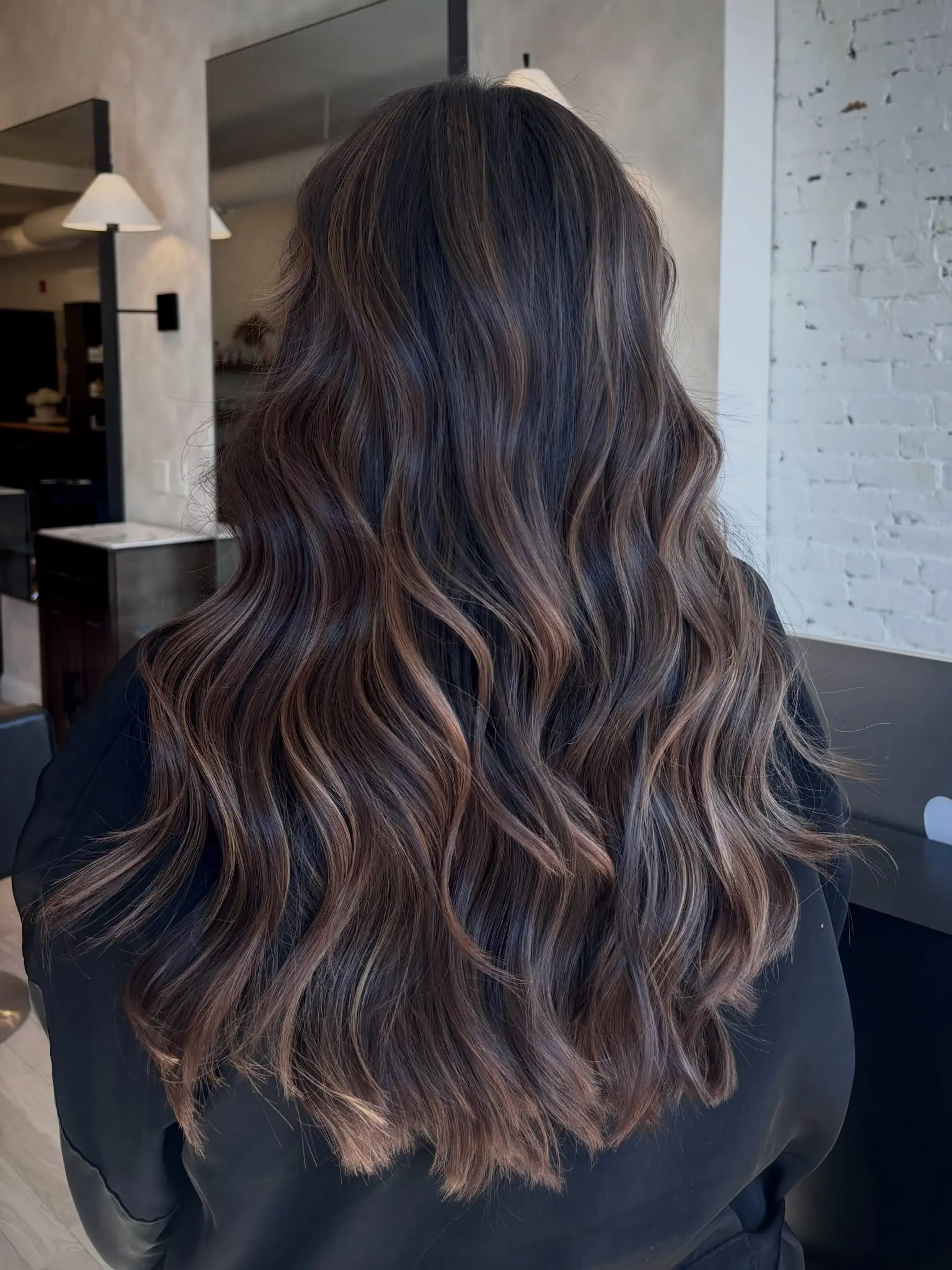 Long chocolate brown hair featuring subtle, dimensional balayage highlights and styled into effortless, cascading waves. 1