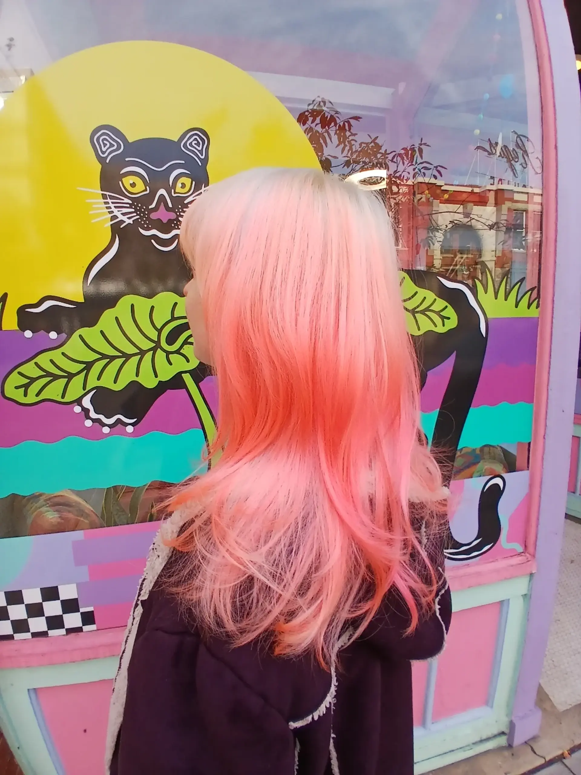 A vivid pastel flamingo pink and peach color melt blended over platinum blonde hair styled in soft waves with bangs. 1