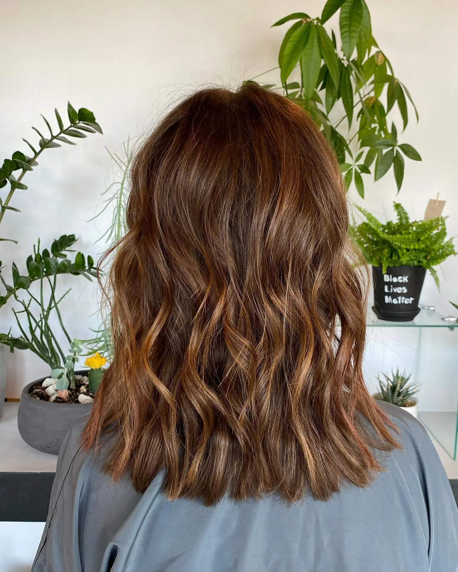 A medium-length lob featuring dimensional warm brown and caramel tones styled in loose, textured waves. 1