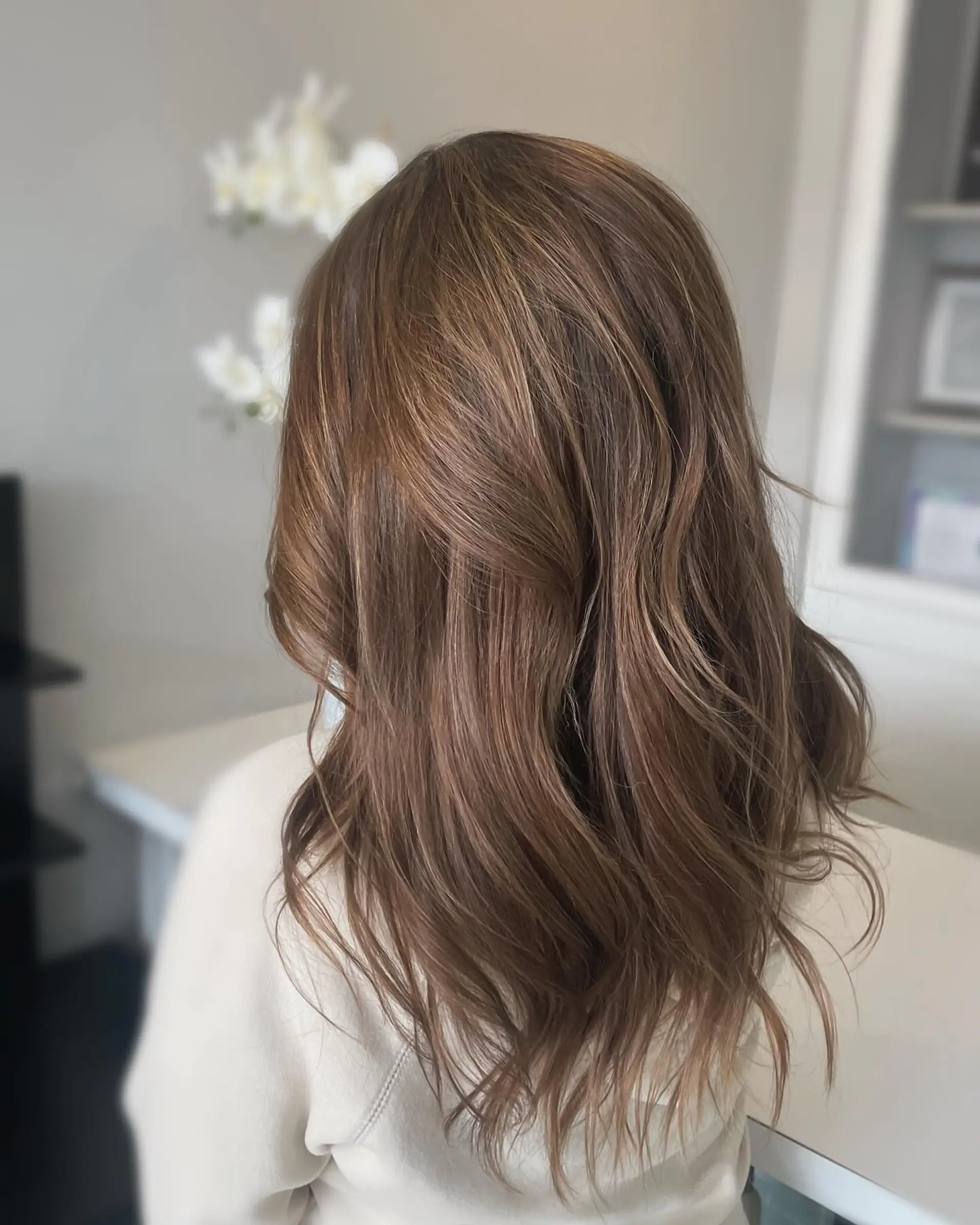 Long layered brunette hair with subtle caramel highlights styled in soft, cascading waves. 1